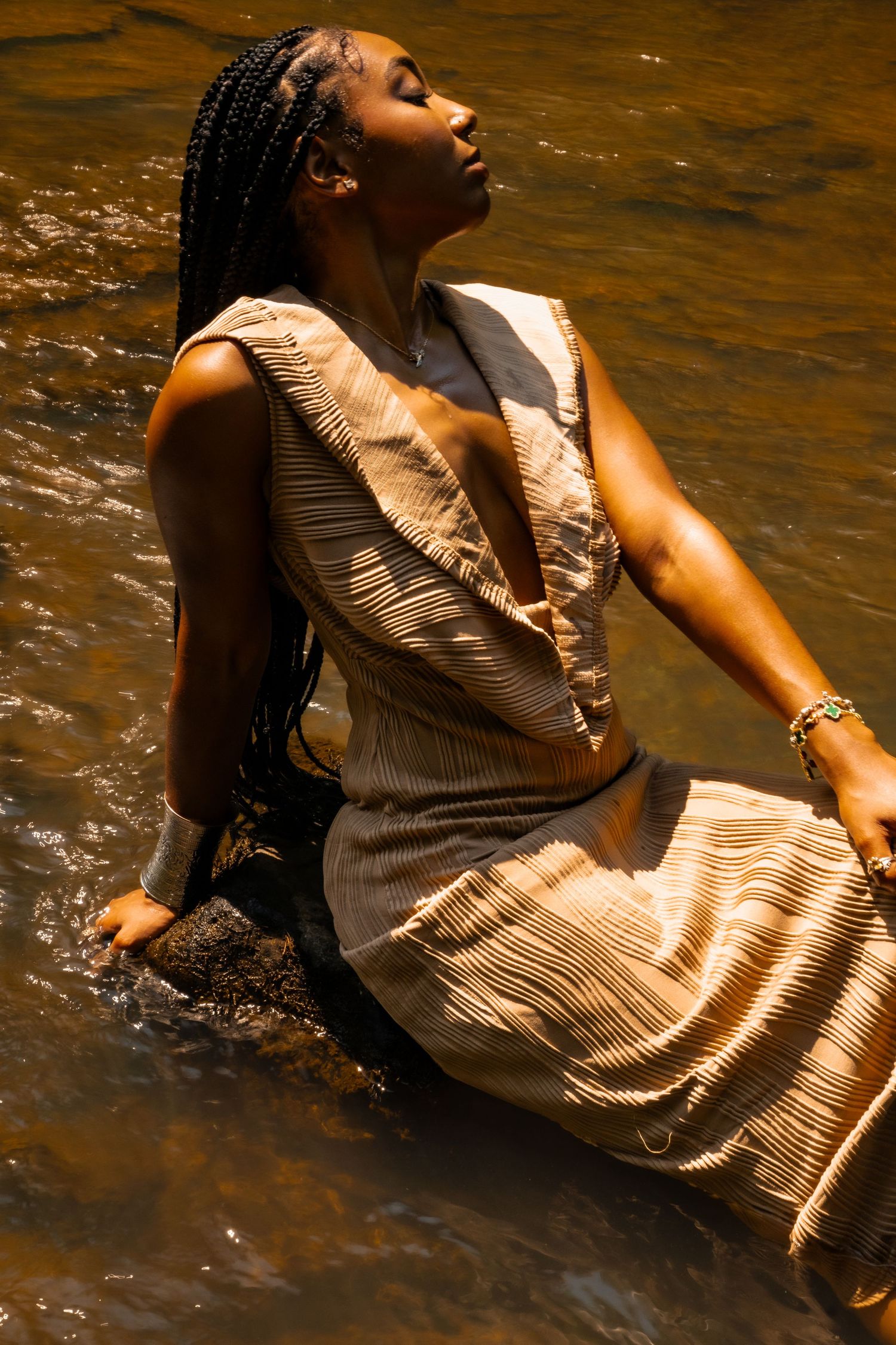 Artistic water portrait featuring flowing beige dress with sunlit reflections on rippling surface.