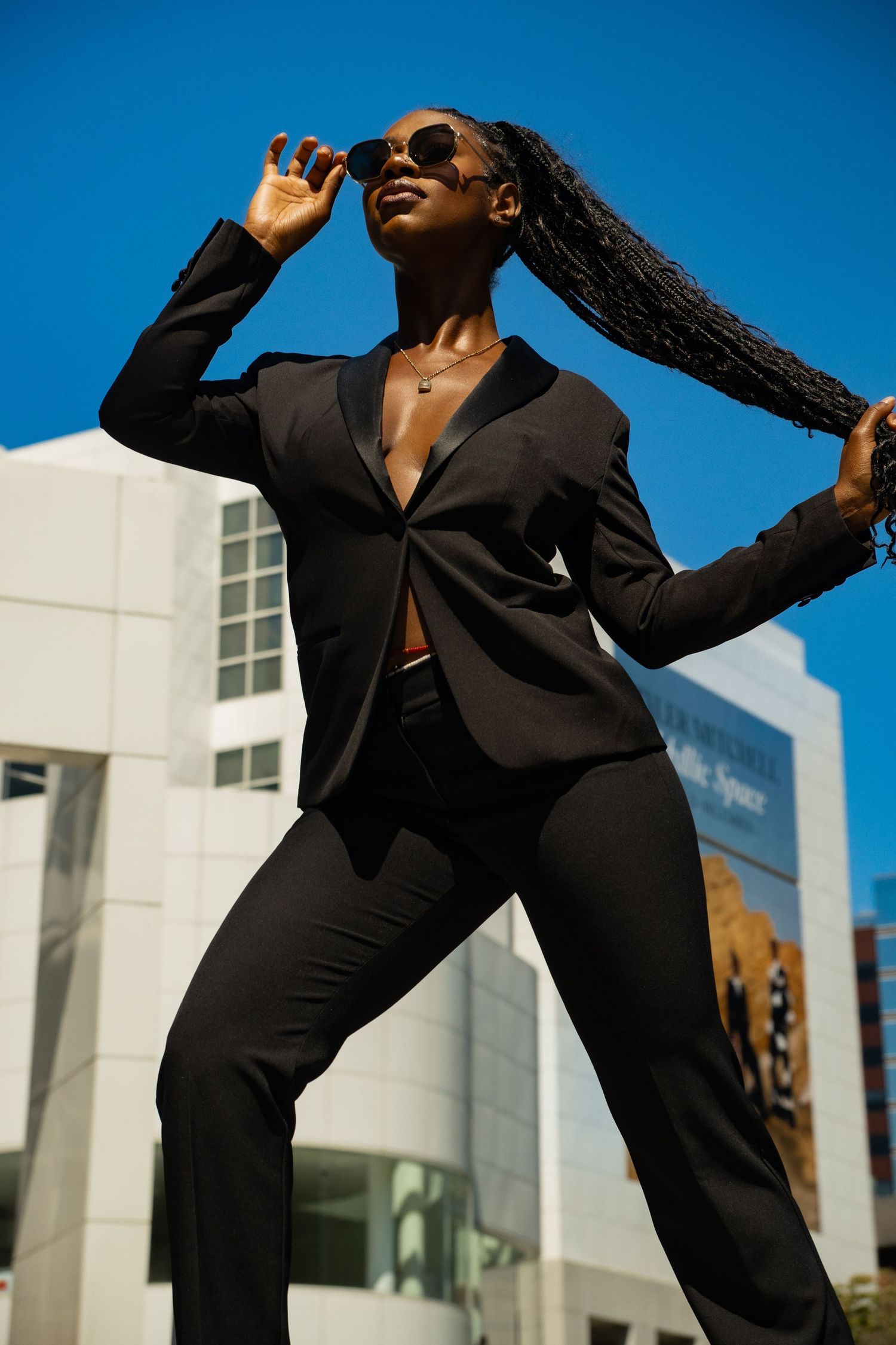 Dynamic fashion shot of person in black suit against bright blue sky.