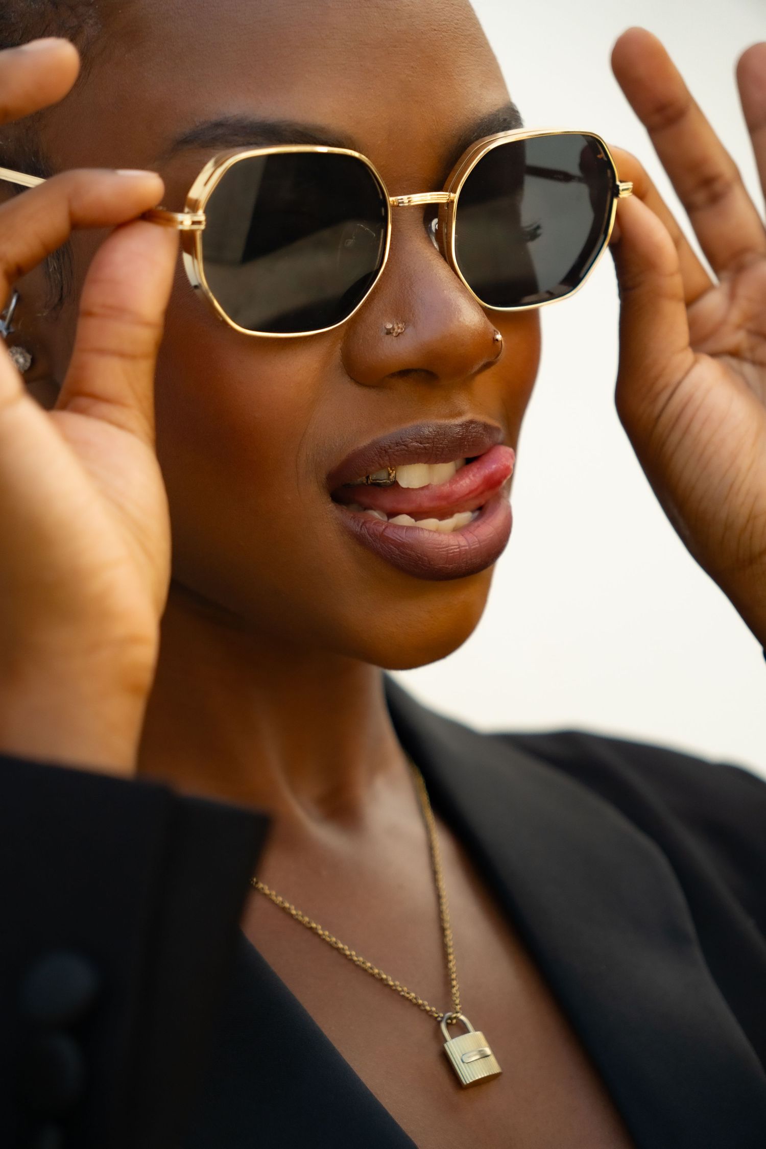 Close-up portrait showcasing gold-framed sunglasses and delicate lock necklace.
