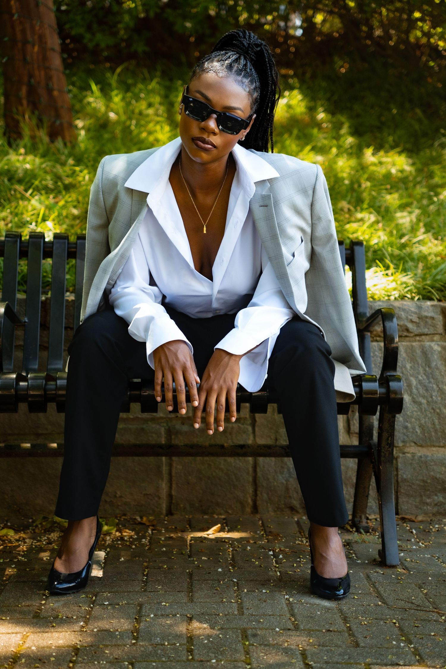 Stylish business outfit featuring a gray blazer, white shirt, and black pants while seated on a park bench in dappled sunlight.