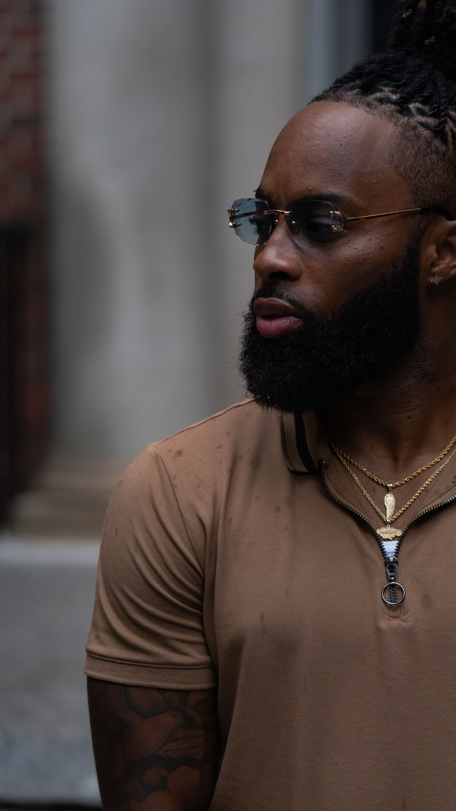 Professional wearing brown polo shirt with glasses and beard in urban setting.