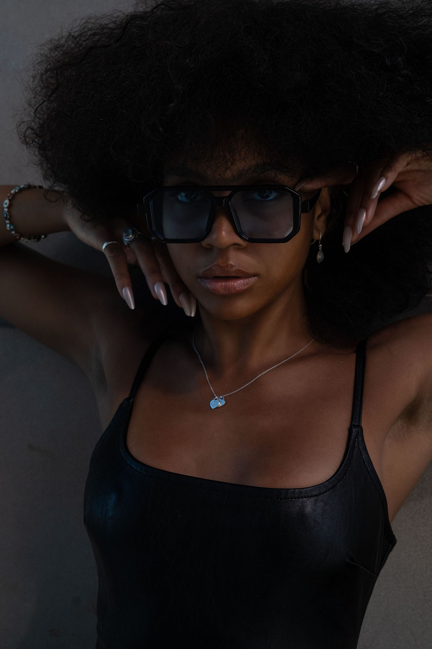 Close-up portraits of a person with natural curly hair and glasses against a dark background.