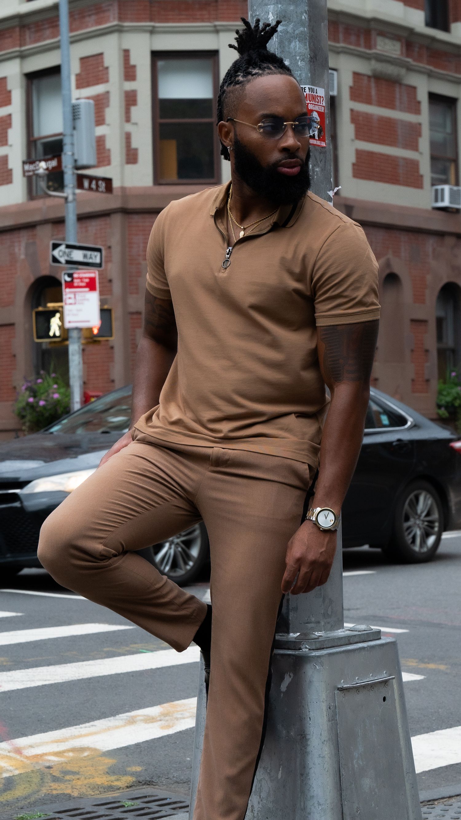 Fashion-forward person in monochrome brown outfit leaning against city pole.