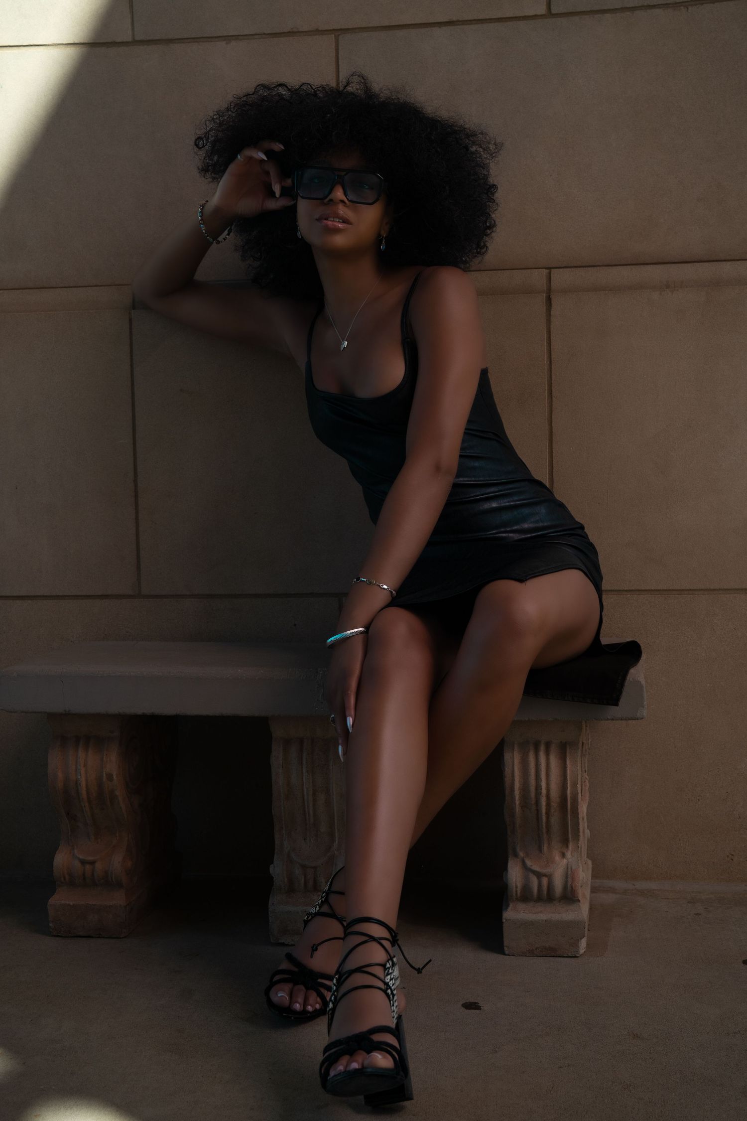 A series of artistic photos showing black strappy sandals and dark clothing against a neutral stone wall background.