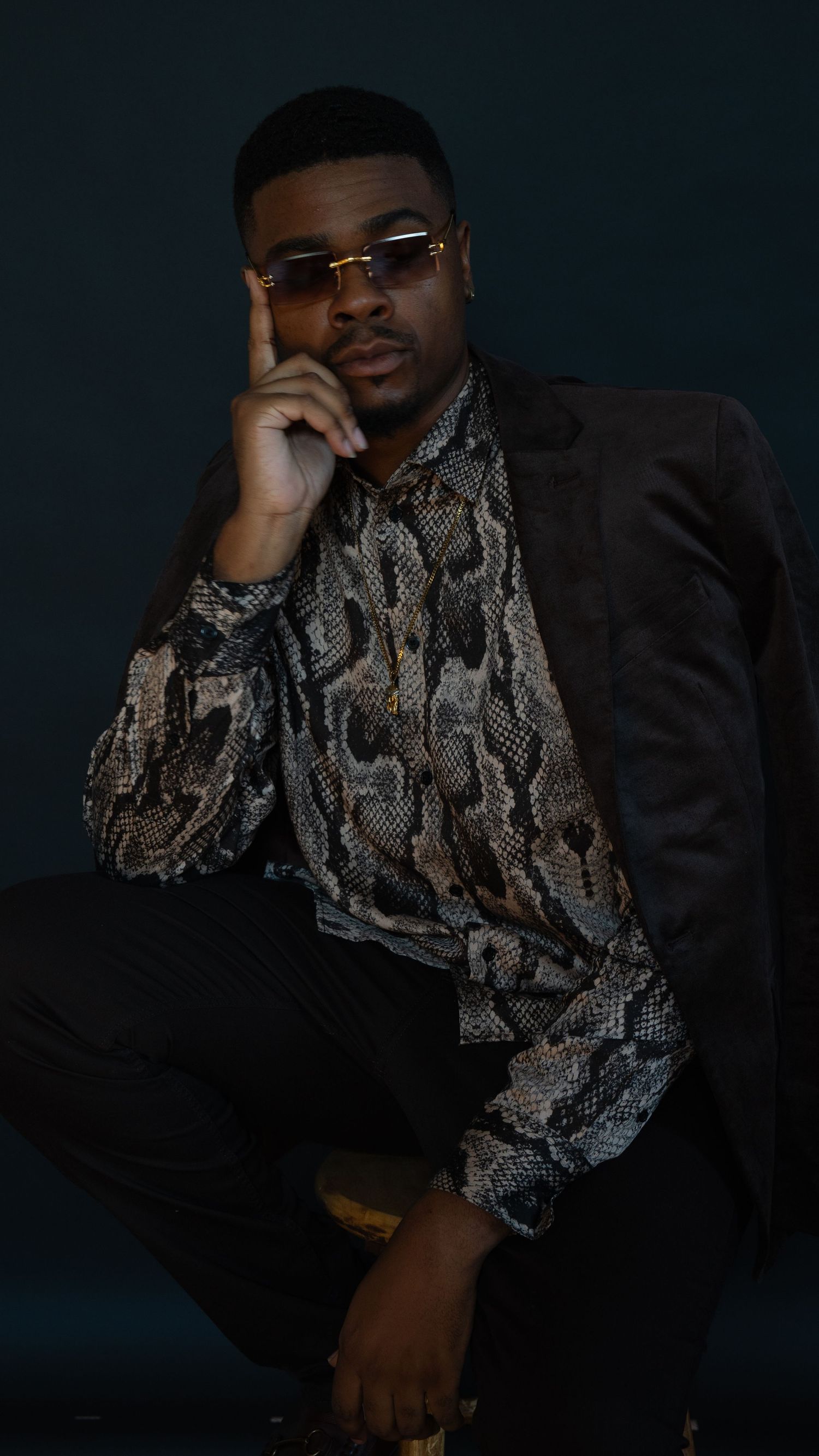 Fashion portrait featuring snakeskin pattern shirt and sunglasses in moody lighting.