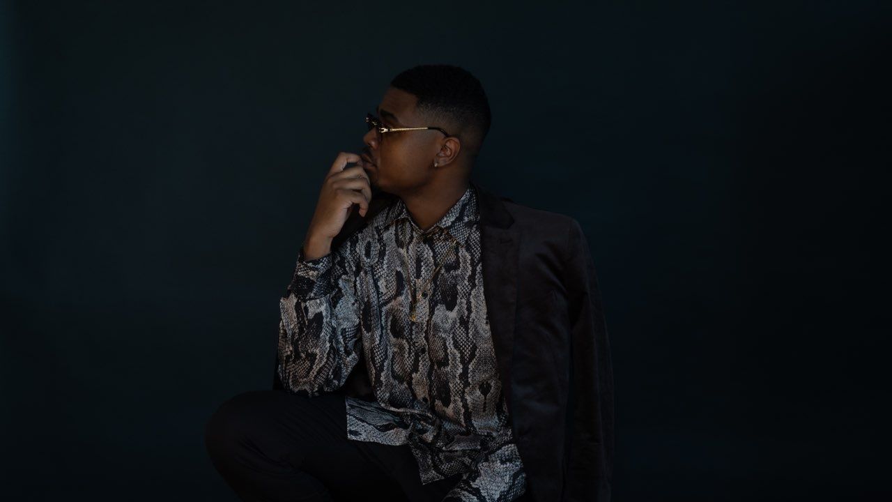 Atmospheric photo of person in snakeskin shirt and blazer against dark backdrop.