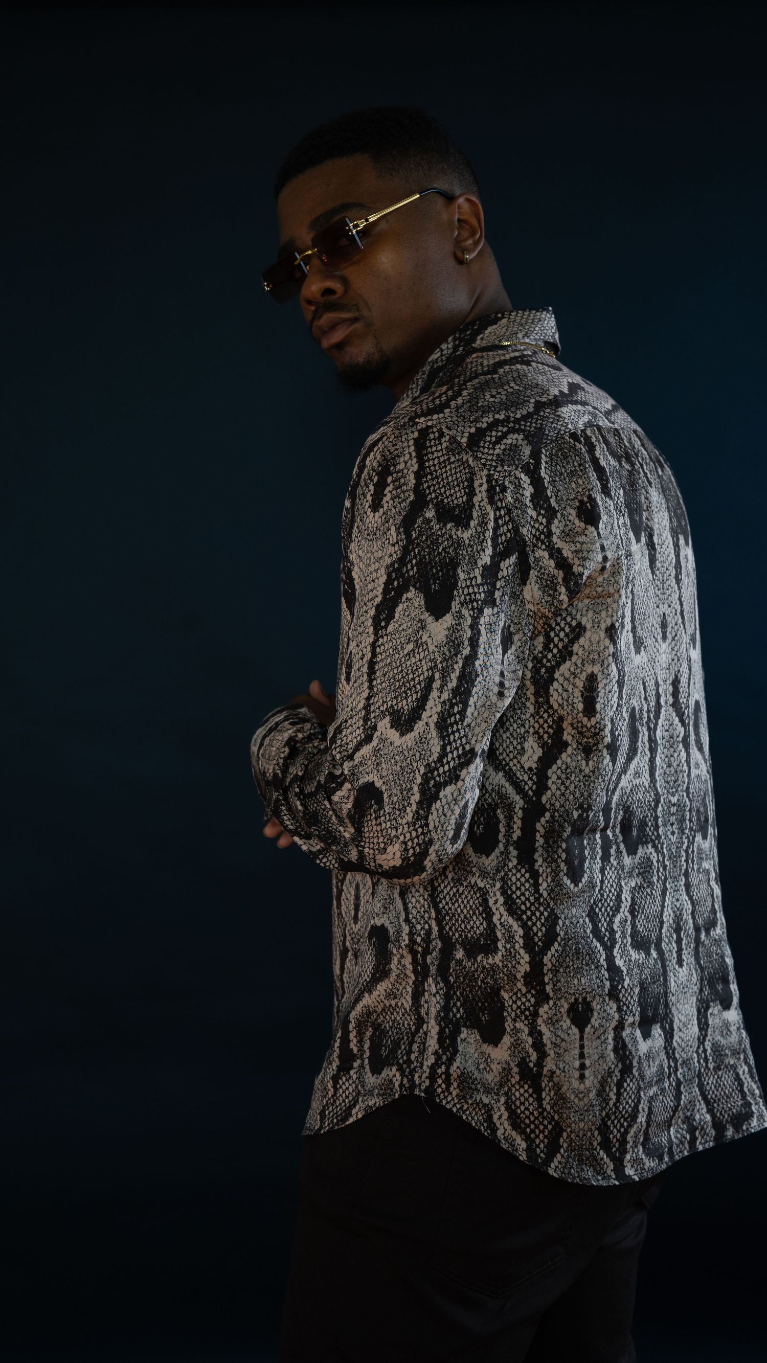 Side profile shot of model wearing textured snakeskin pattern shirt in dark studio setting.