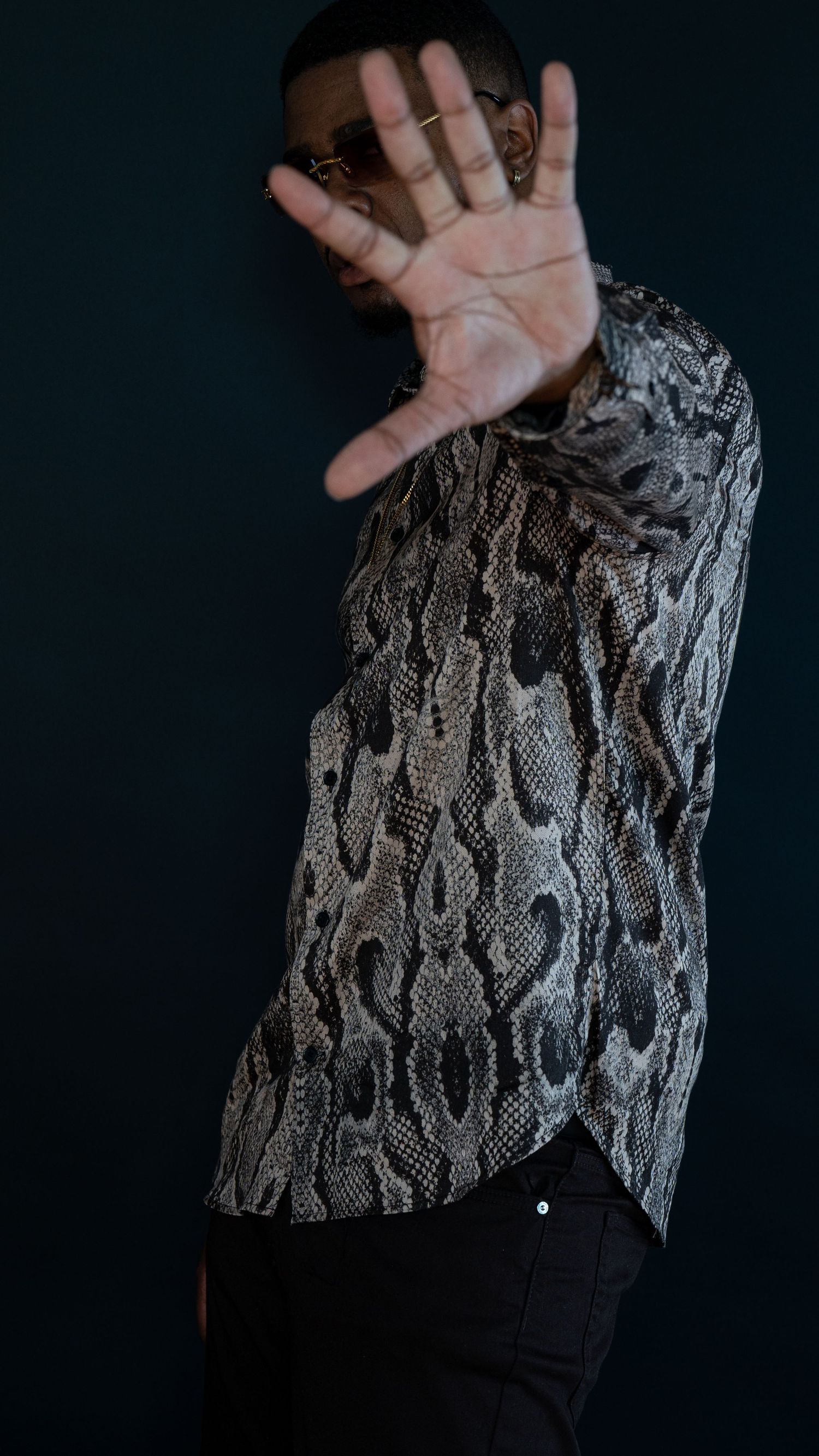 Hand gesture photograph with snakeskin print shirt against dark background.