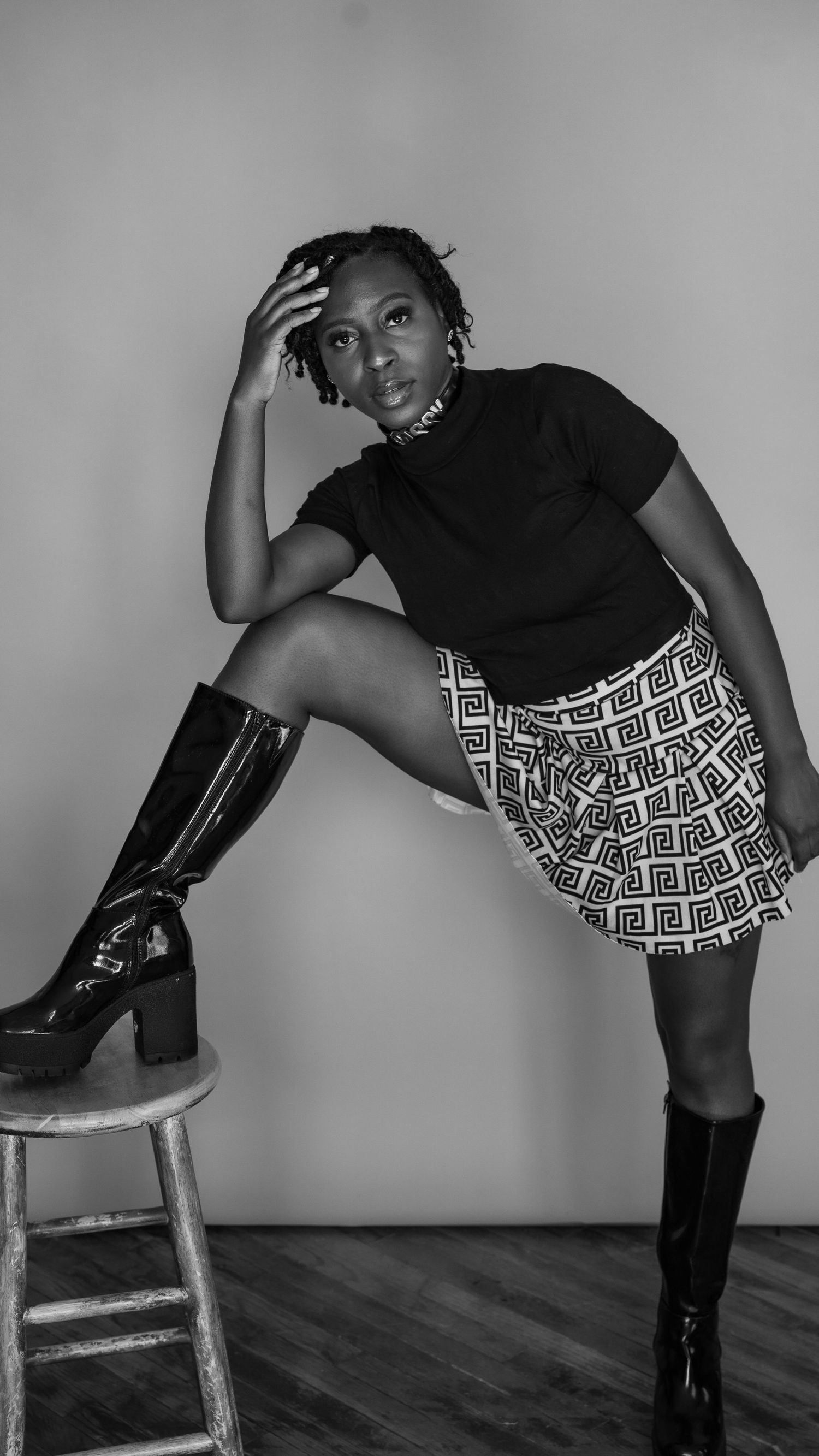 Dynamic black and white portrait with boots and patterned skirt against studio backdrop.