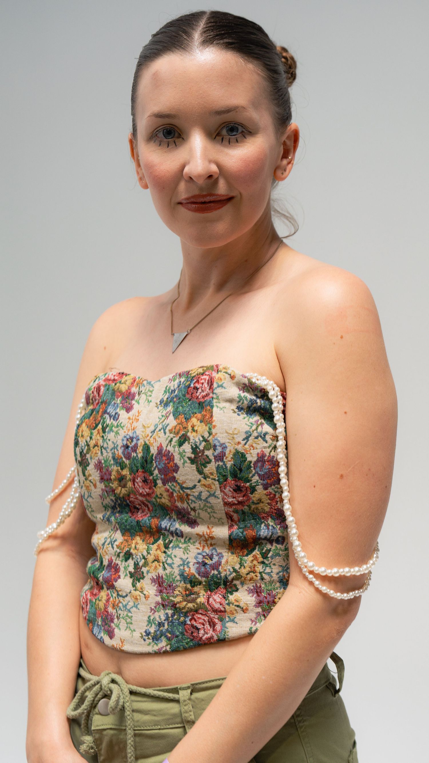 Portrait of model wearing floral corset top with pearl details against grey background.