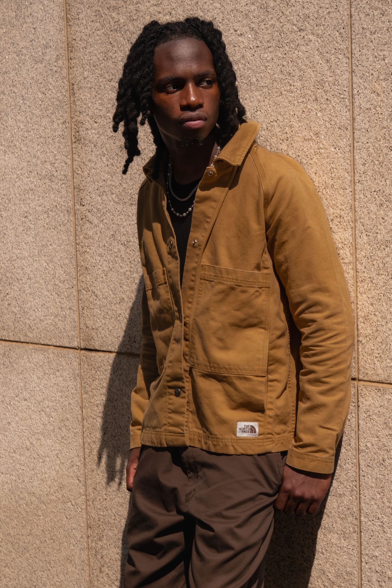 Fashion portrait featuring tan workwear jacket against textured wall background.