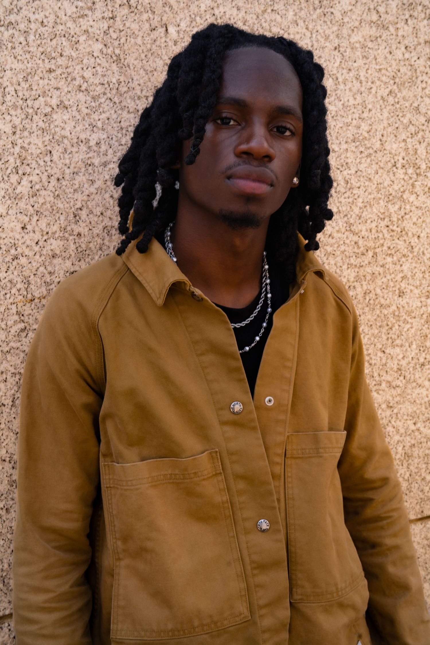 Portrait showcasing casual style with brown jacket and silver chain necklace.