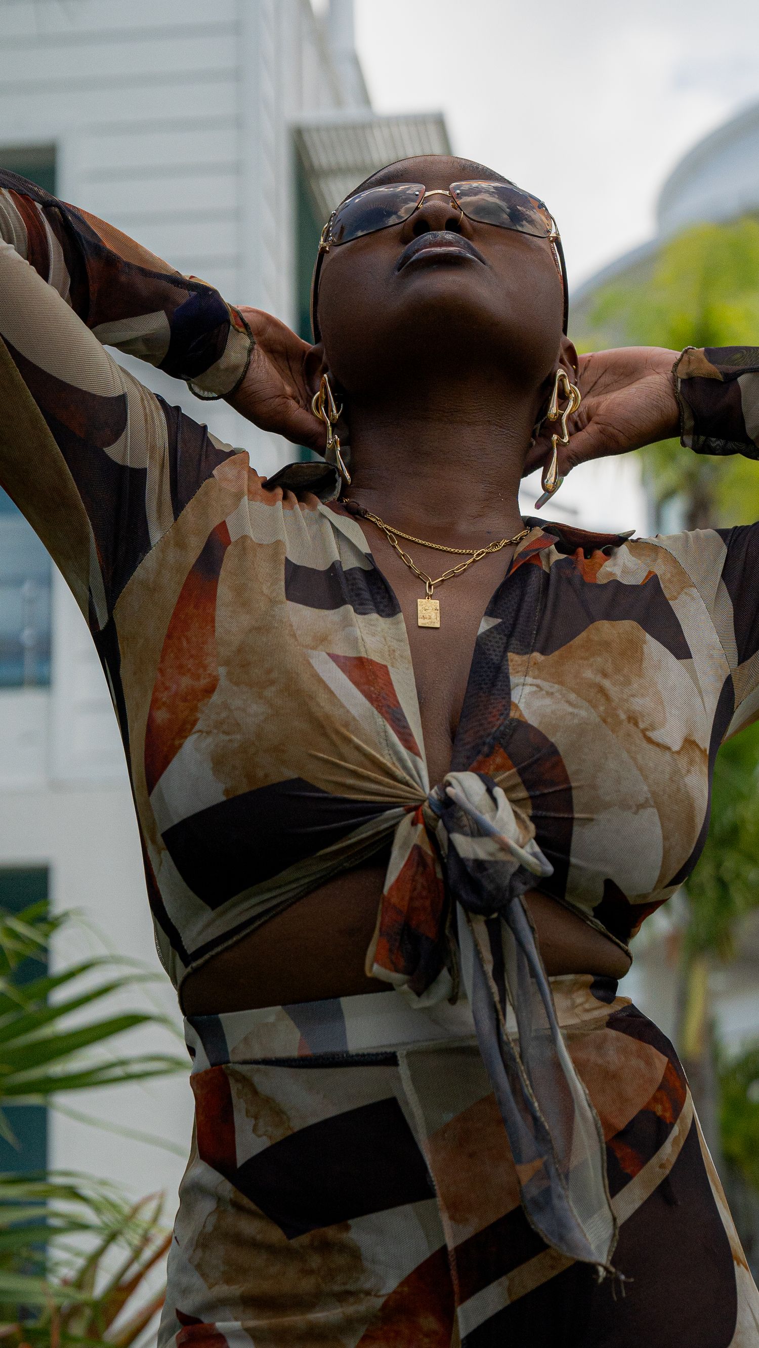 Model in abstract print wrap top poses against tropical foliage background.