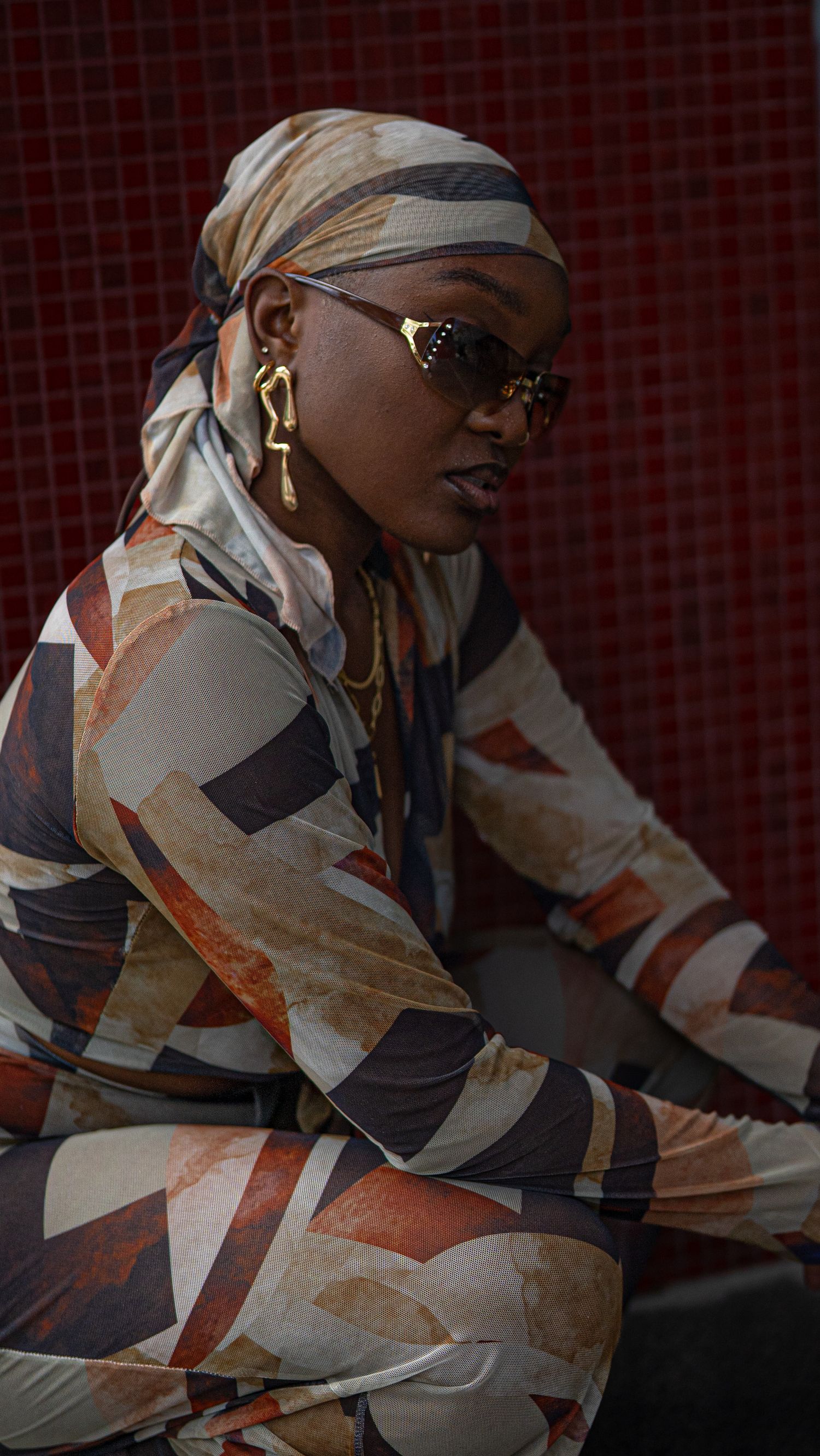 Fashion model in geometric print outfit poses against textured red background.