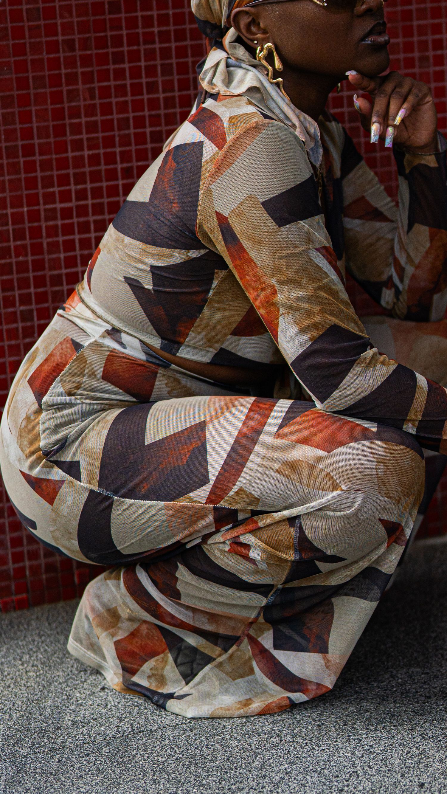 Side view of model in flowing abstract print ensemble against red tiled backdrop.