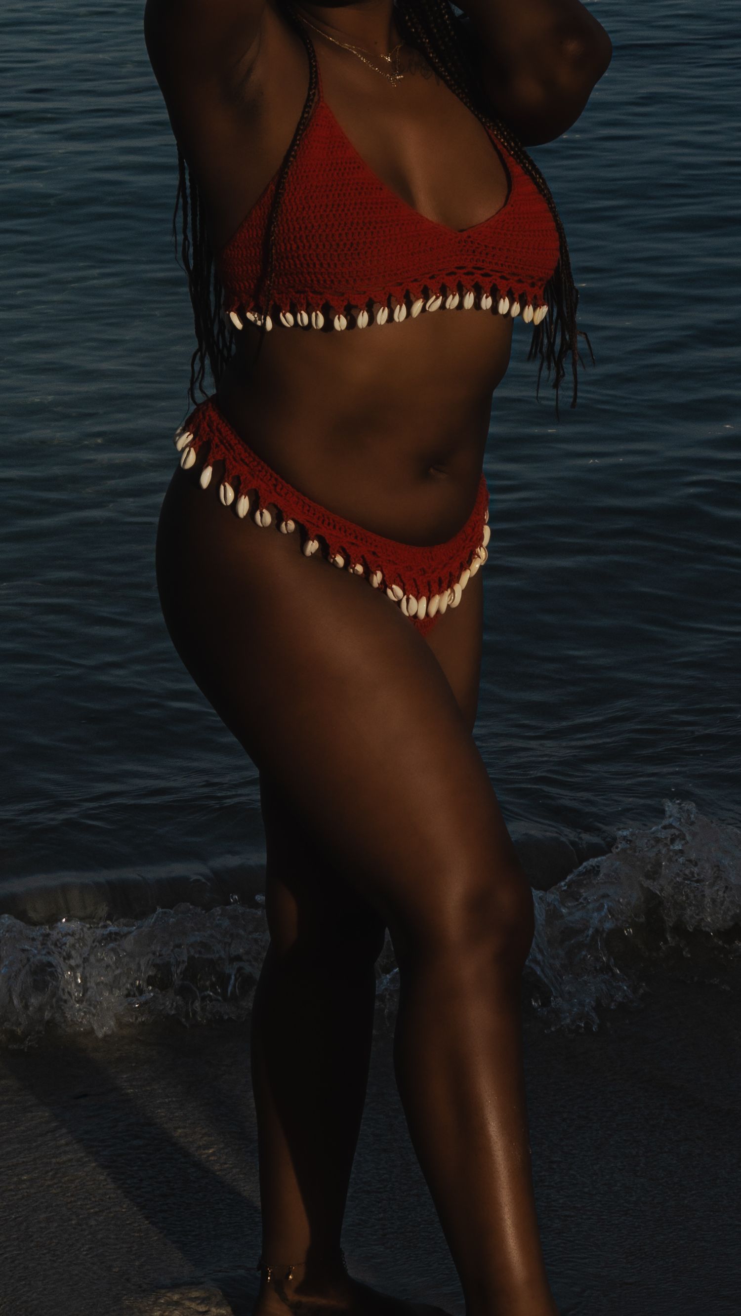 Red bikini adorned with seashells photographed against dark ocean waters at beach.
