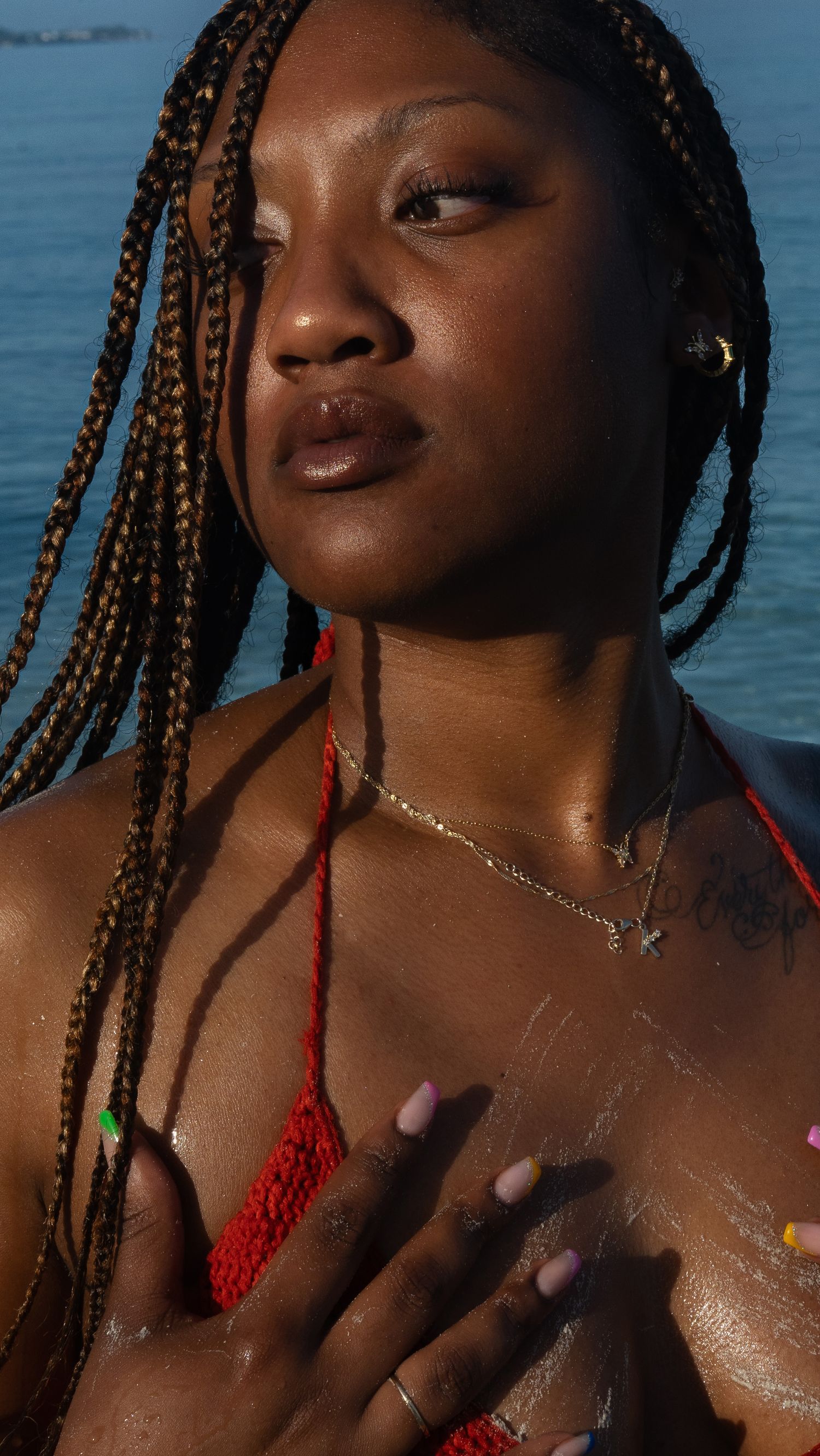 Beautiful portrait by the water featuring braided hair, red swimwear, and delicate necklace details in warm sunlight.