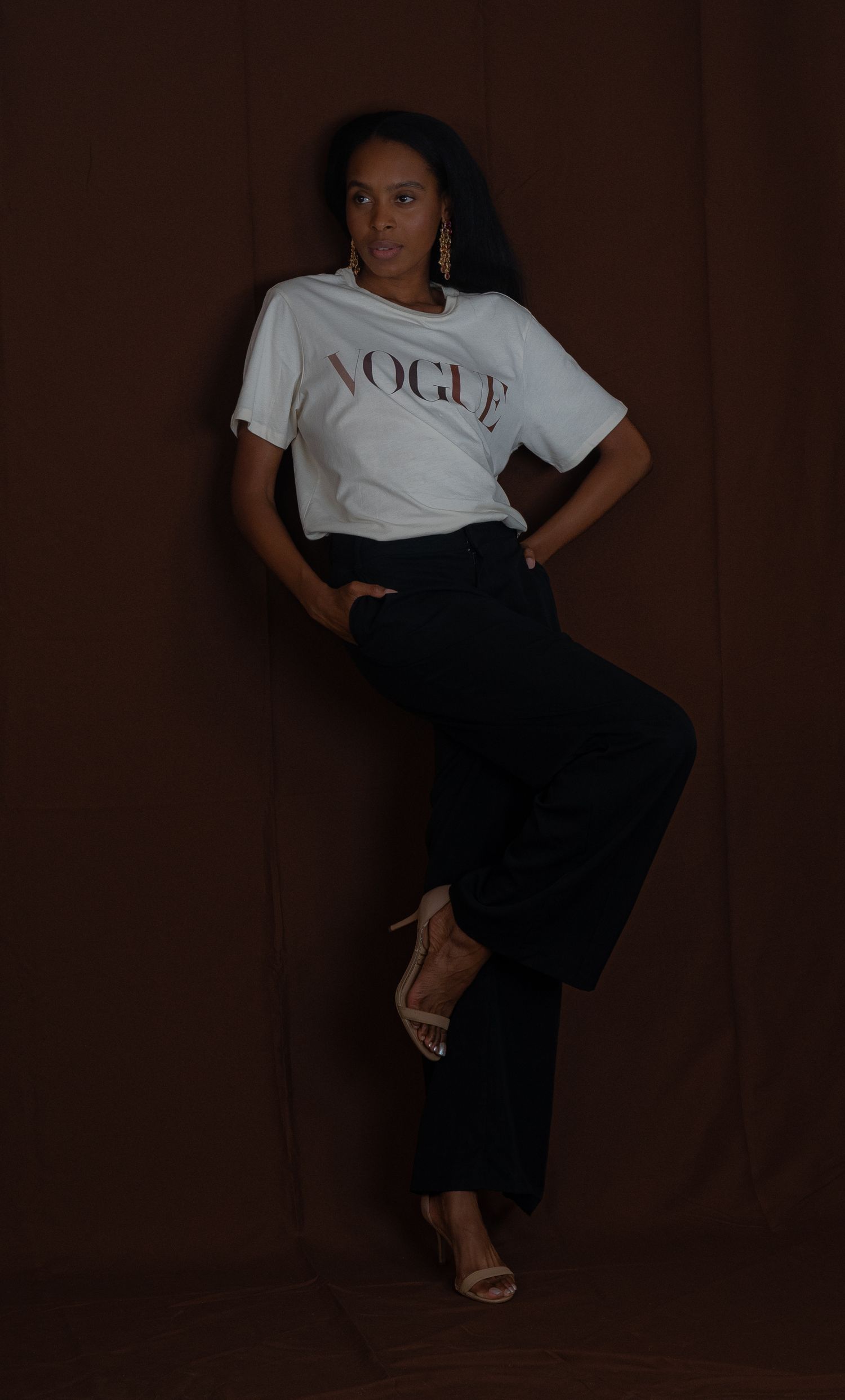 A moody portrait showing a casual Vogue t-shirt and wide-leg pants combination against brown backdrop.
