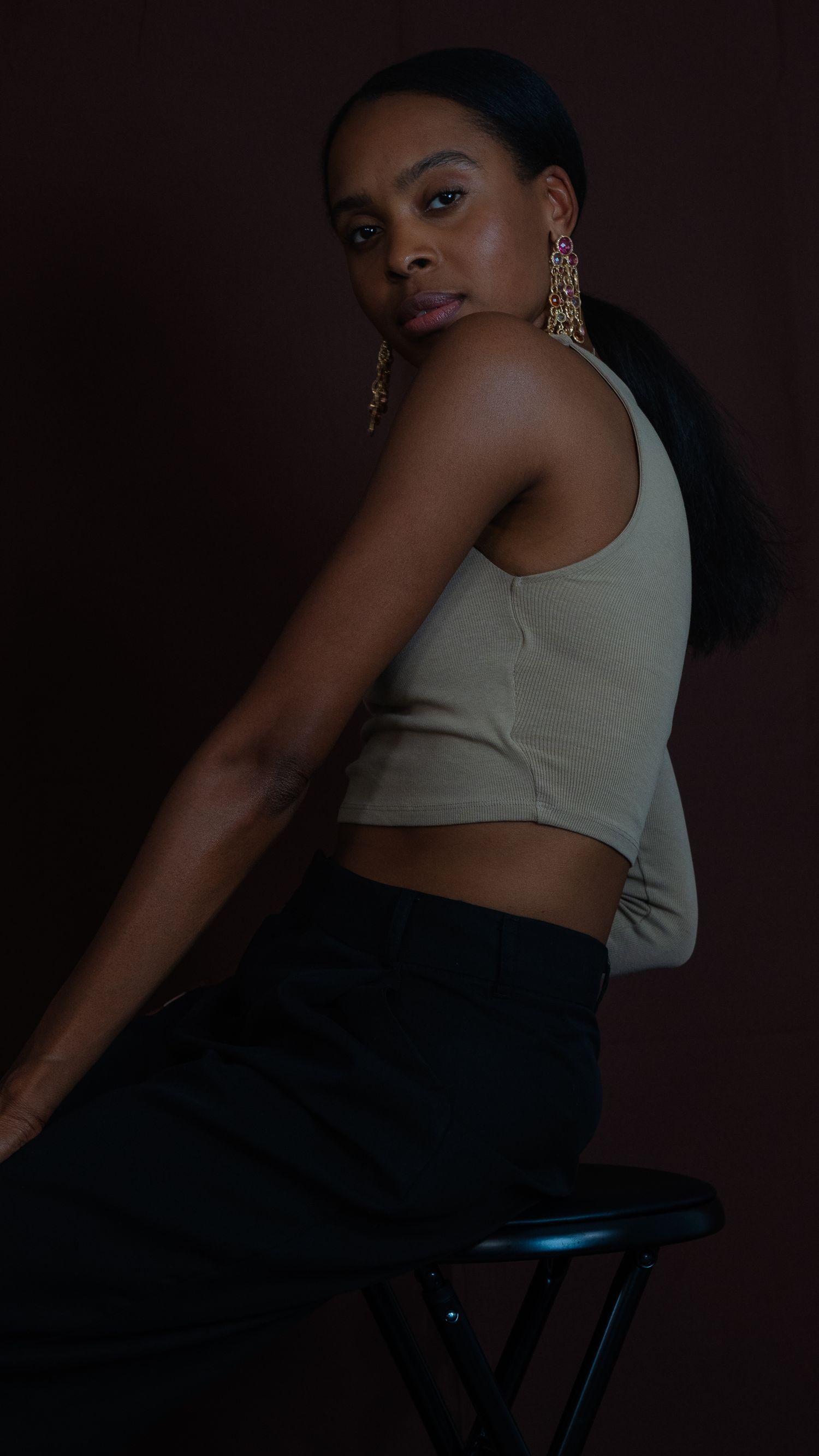 A moody studio portrait featuring a beige crop top and statement earrings against dark background.
