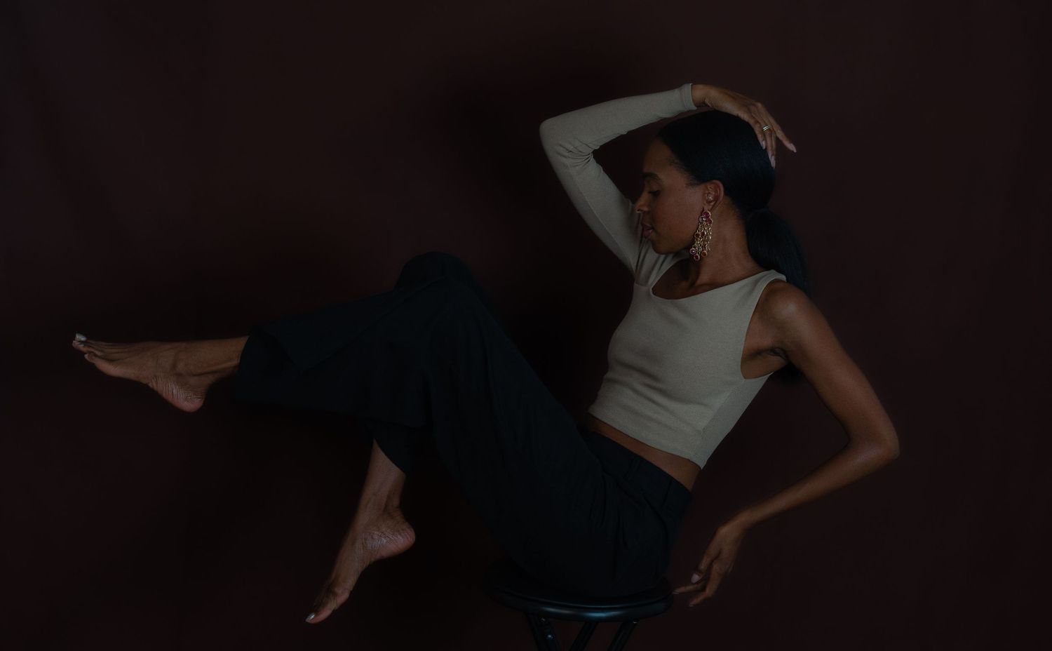 Athletic dancer in white tank top and dark pants poses on floor in moody low-light artistic portrait.