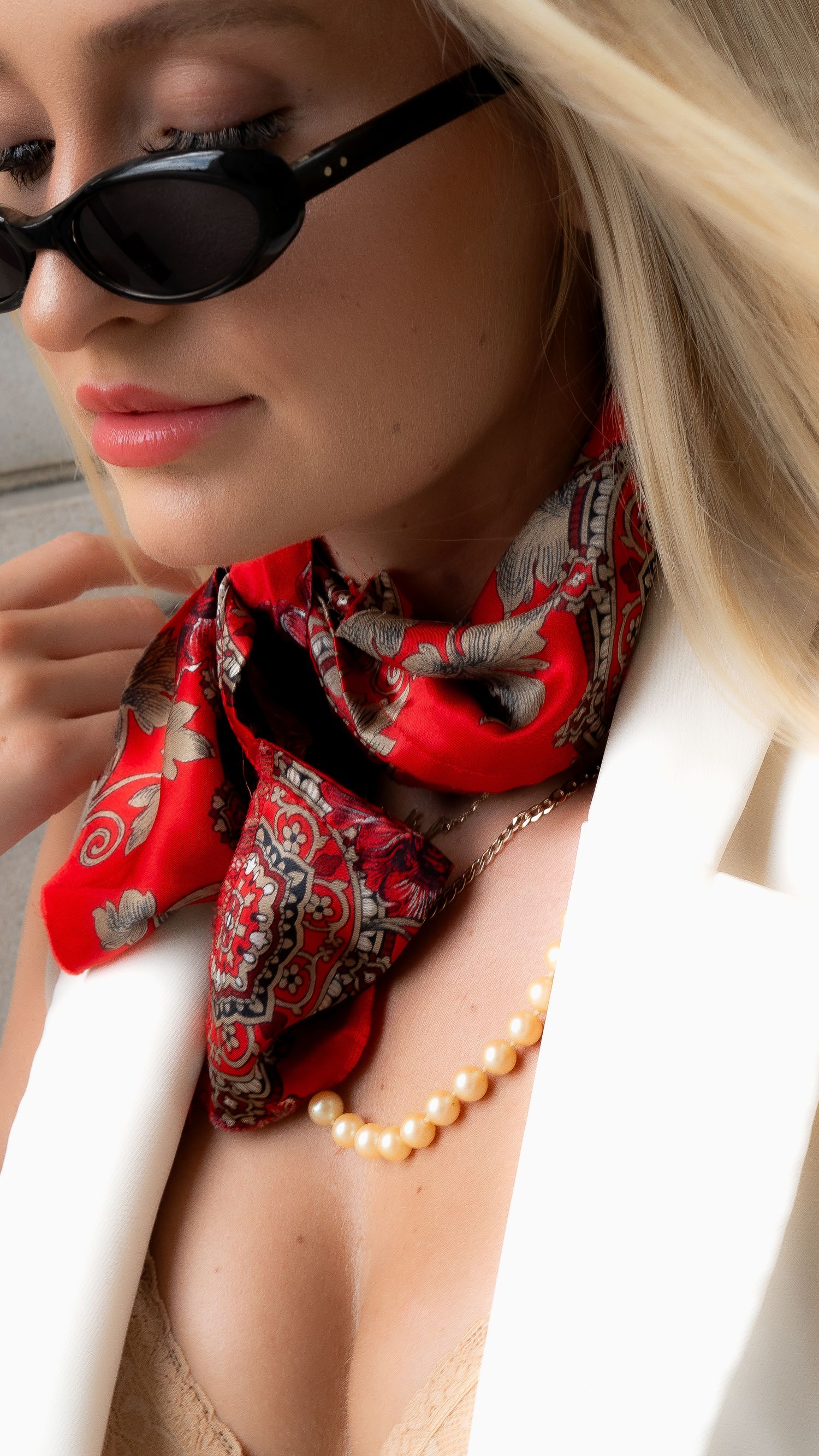 Fashion detail of red silk scarf, pearl necklace and sunglasses with white blazer.