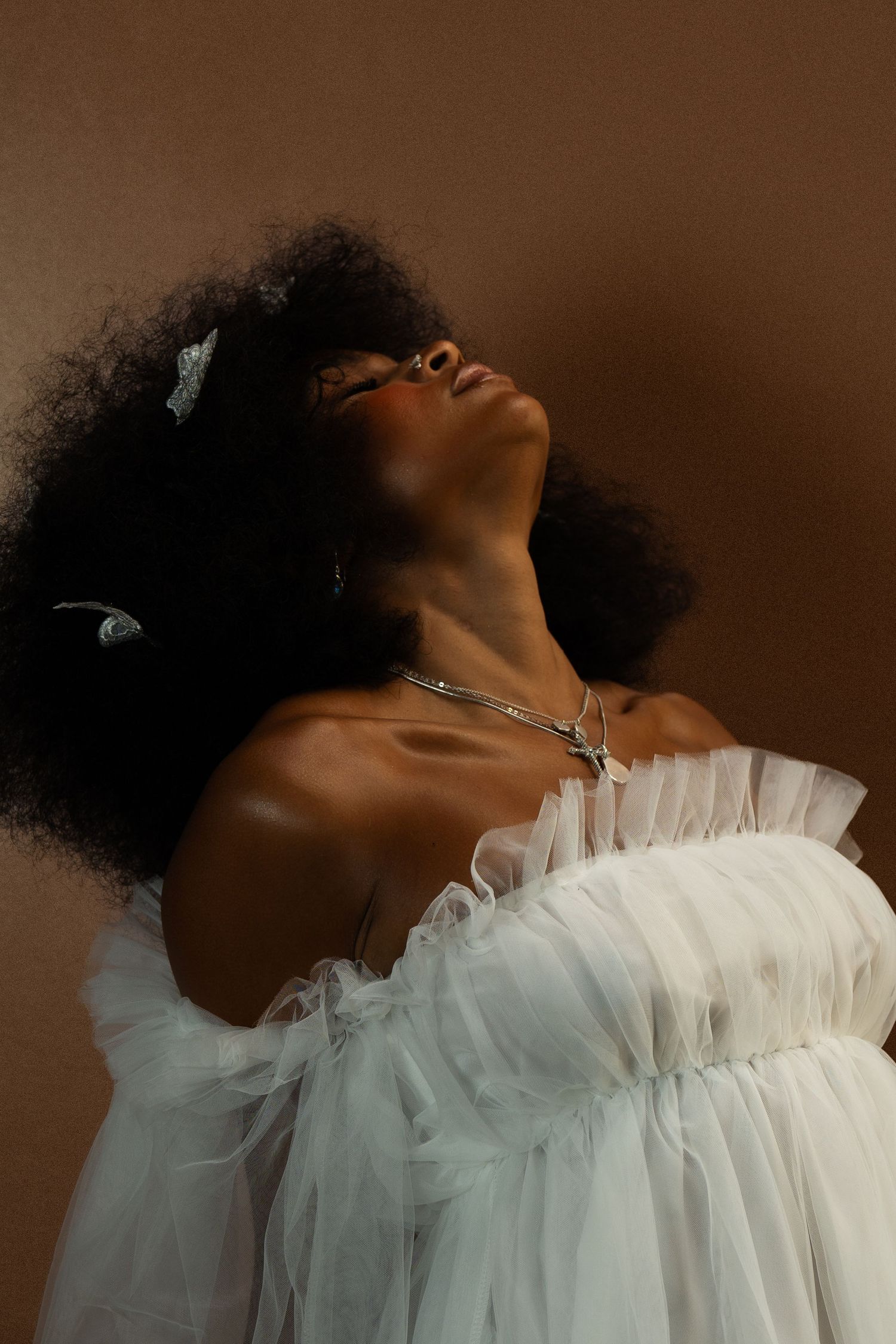 Ethereal fashion portrait featuring flowing white tulle dress and natural afro hair adorned with delicate butterflies.