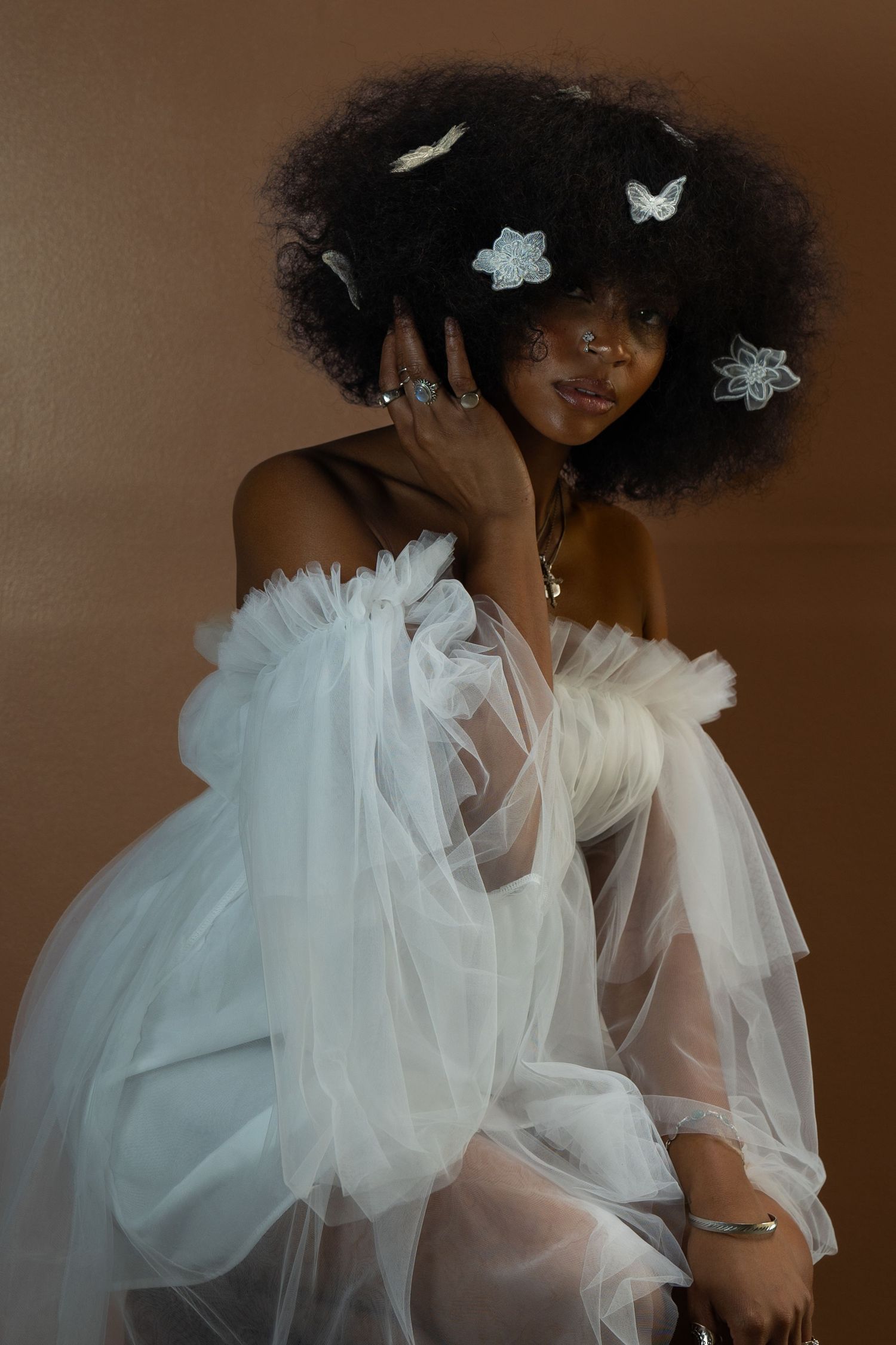 Dreamy portrait with natural afro adorned with silver butterflies and off-shoulder white tulle gown.