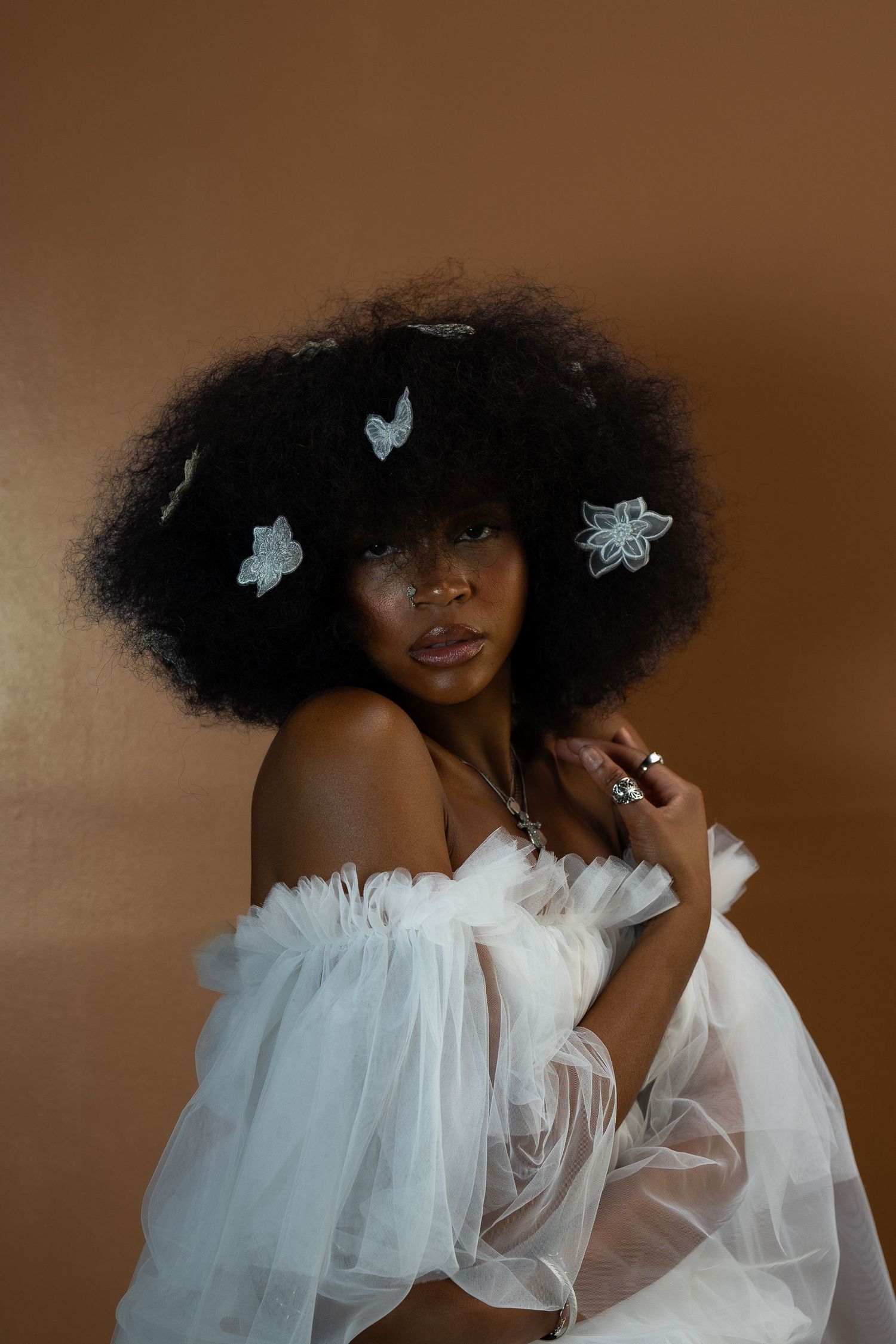 Elegant beauty shot showcasing natural afro decorated with silver butterflies and white ruffled dress.