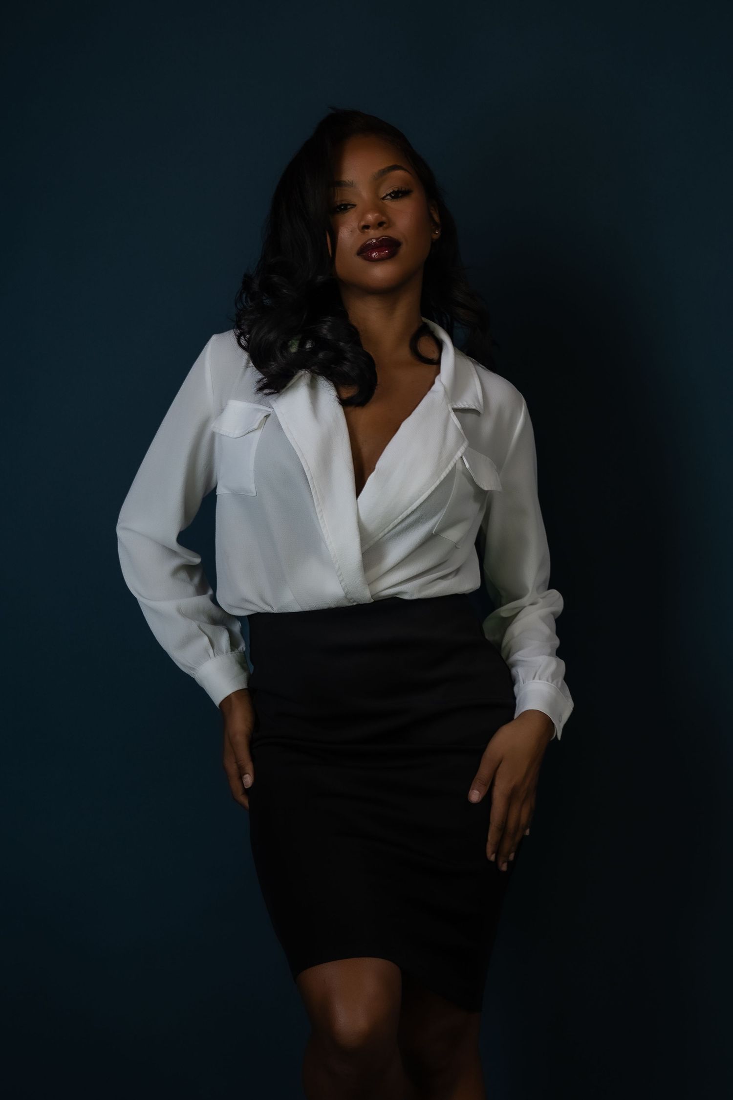 Professional portrait of a person in a white blouse and black pencil skirt against a dark background.
