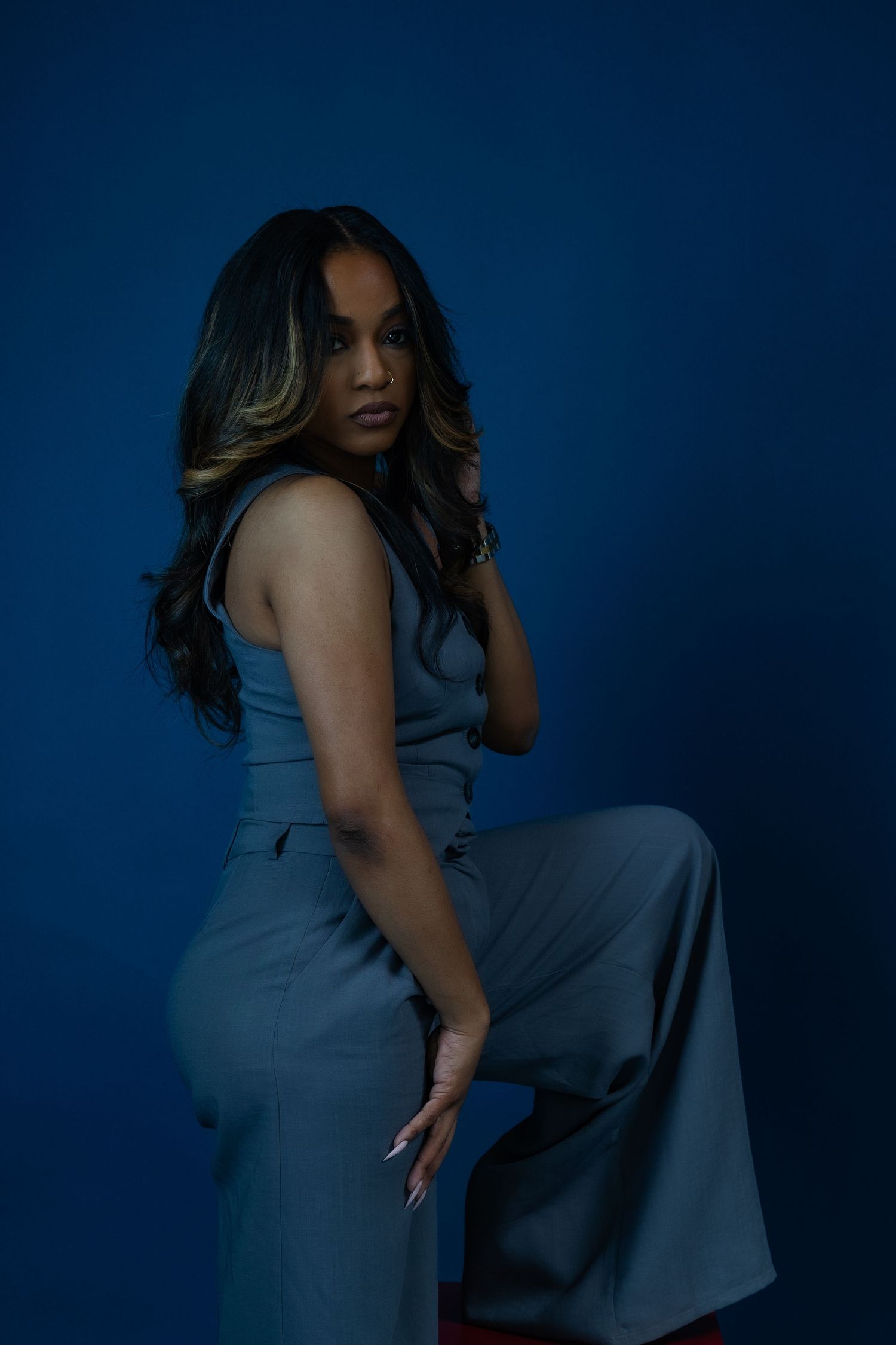 Fashion portrait of model in blue outfit posing against dark blue background.