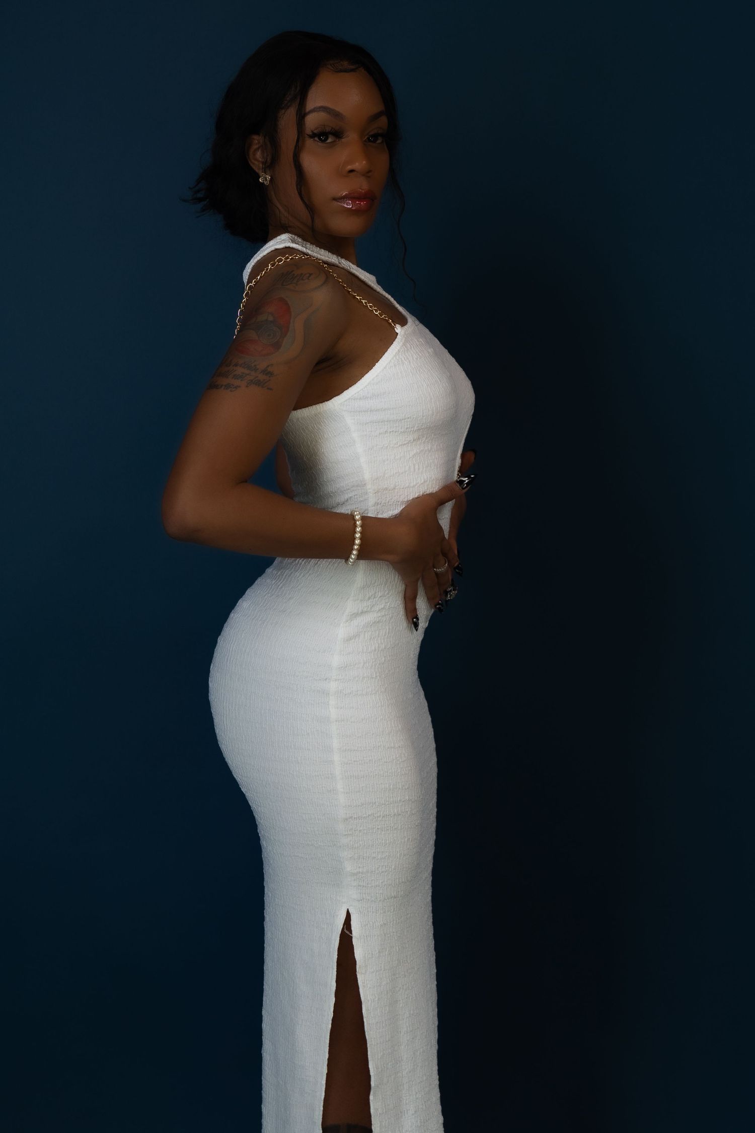 Fashion portrait in form-fitting white dress with side slit against dark blue background.