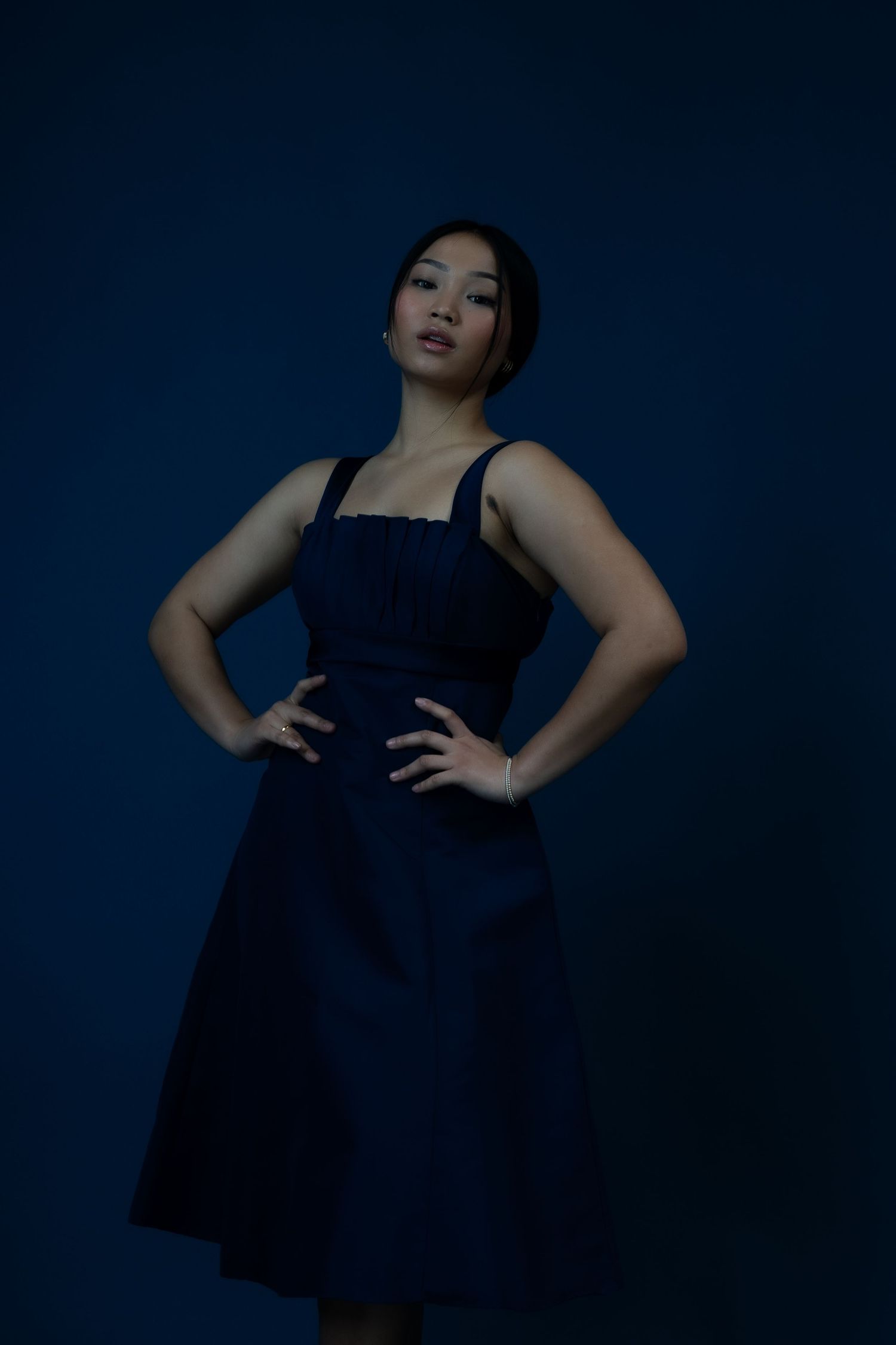 Dramatic fashion portrait of a model in a navy blue dress against a dark blue background.