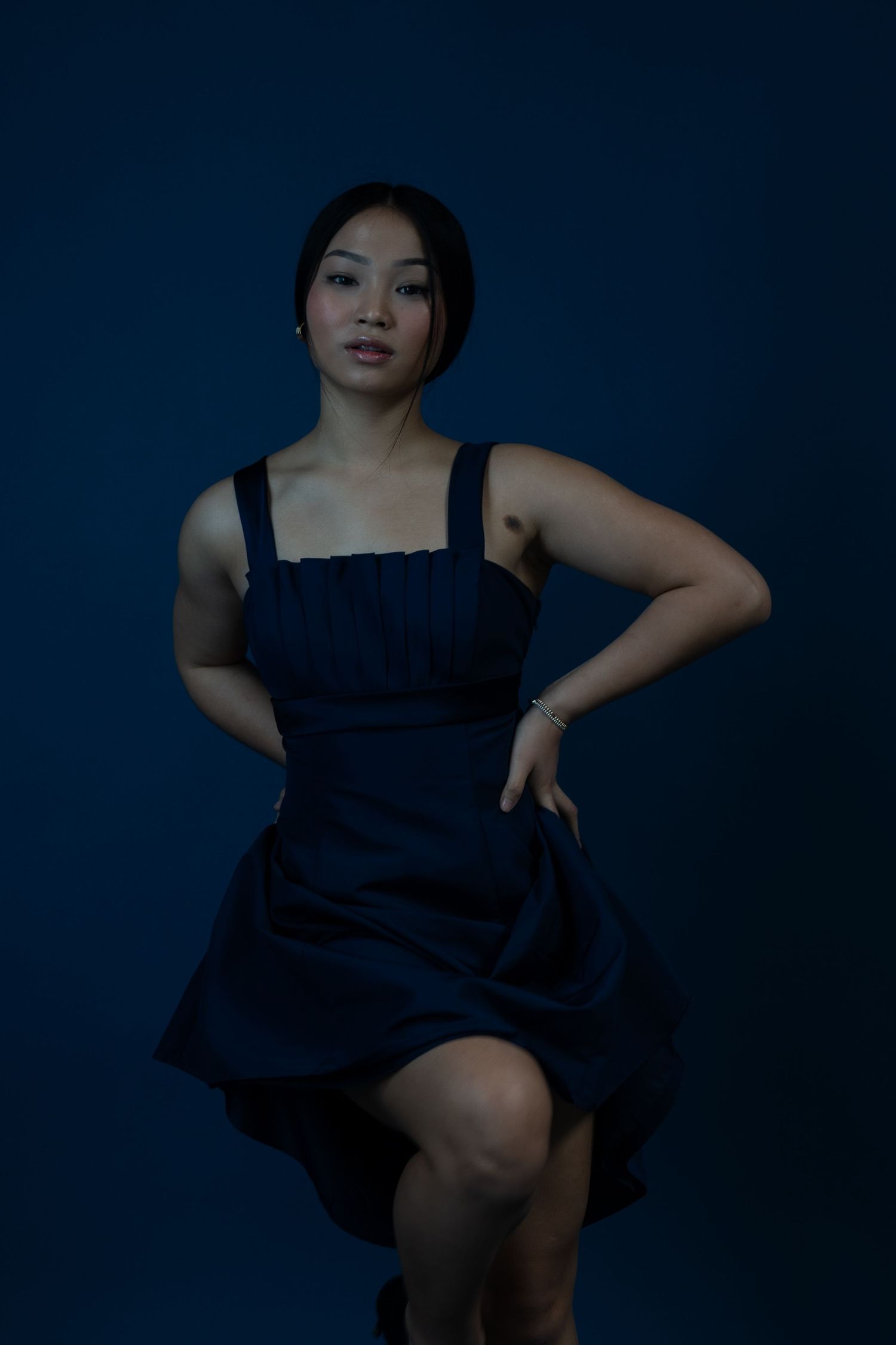Dynamic movement captured as model twirls in navy dress against dark background.