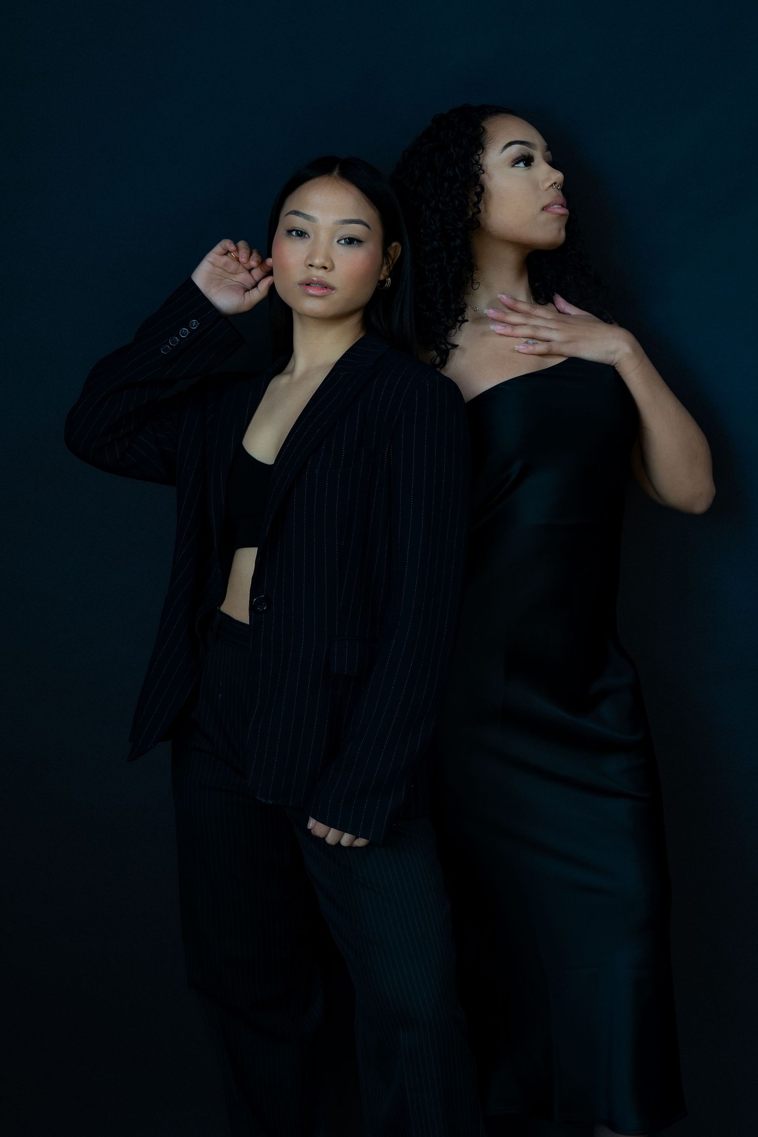 Fashion models in black attire strike artistic poses against dark backdrop.
