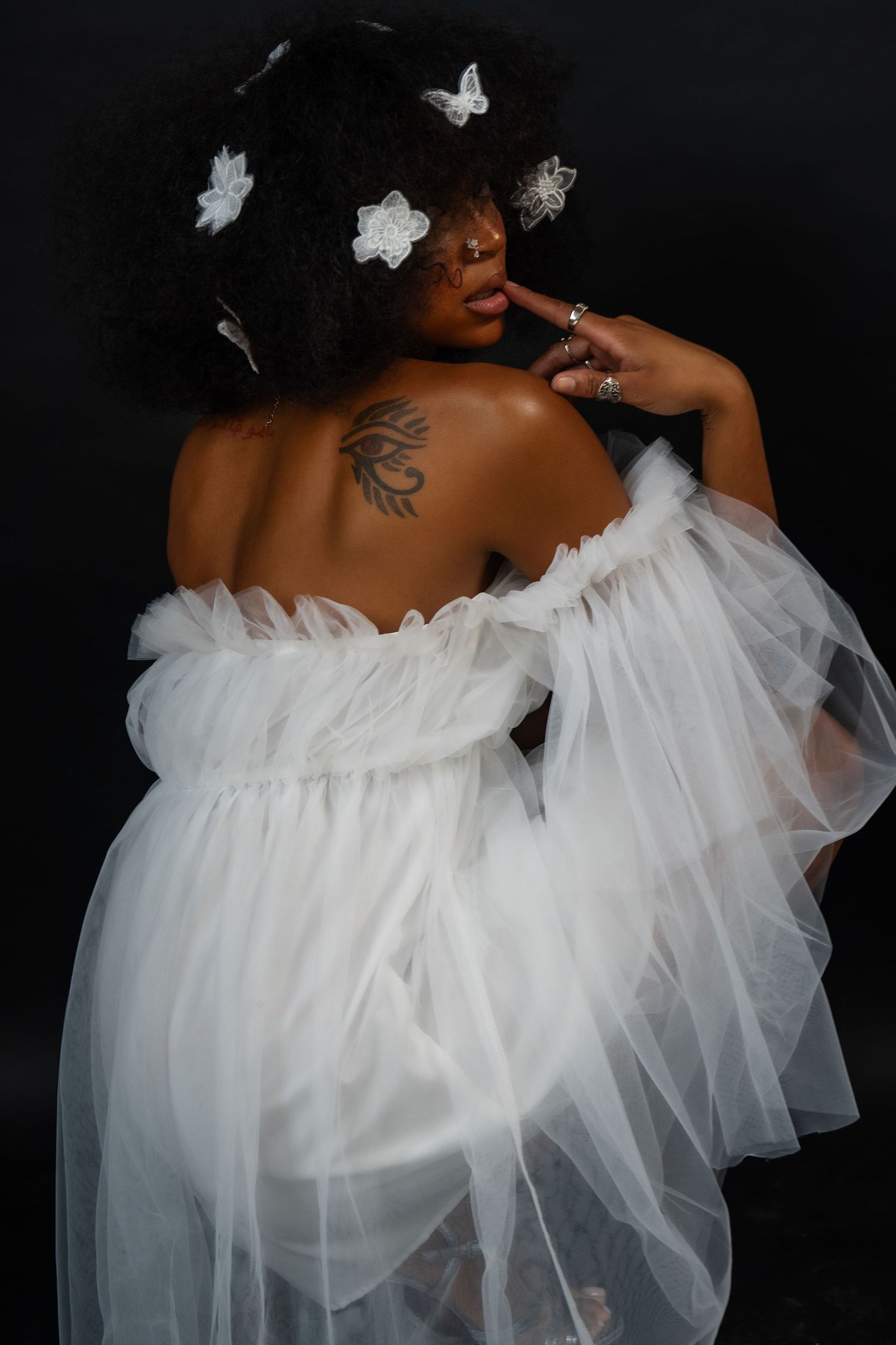 Back view portrait showing tattoo detail and white tulle dress with silver butterfly hair accessories.