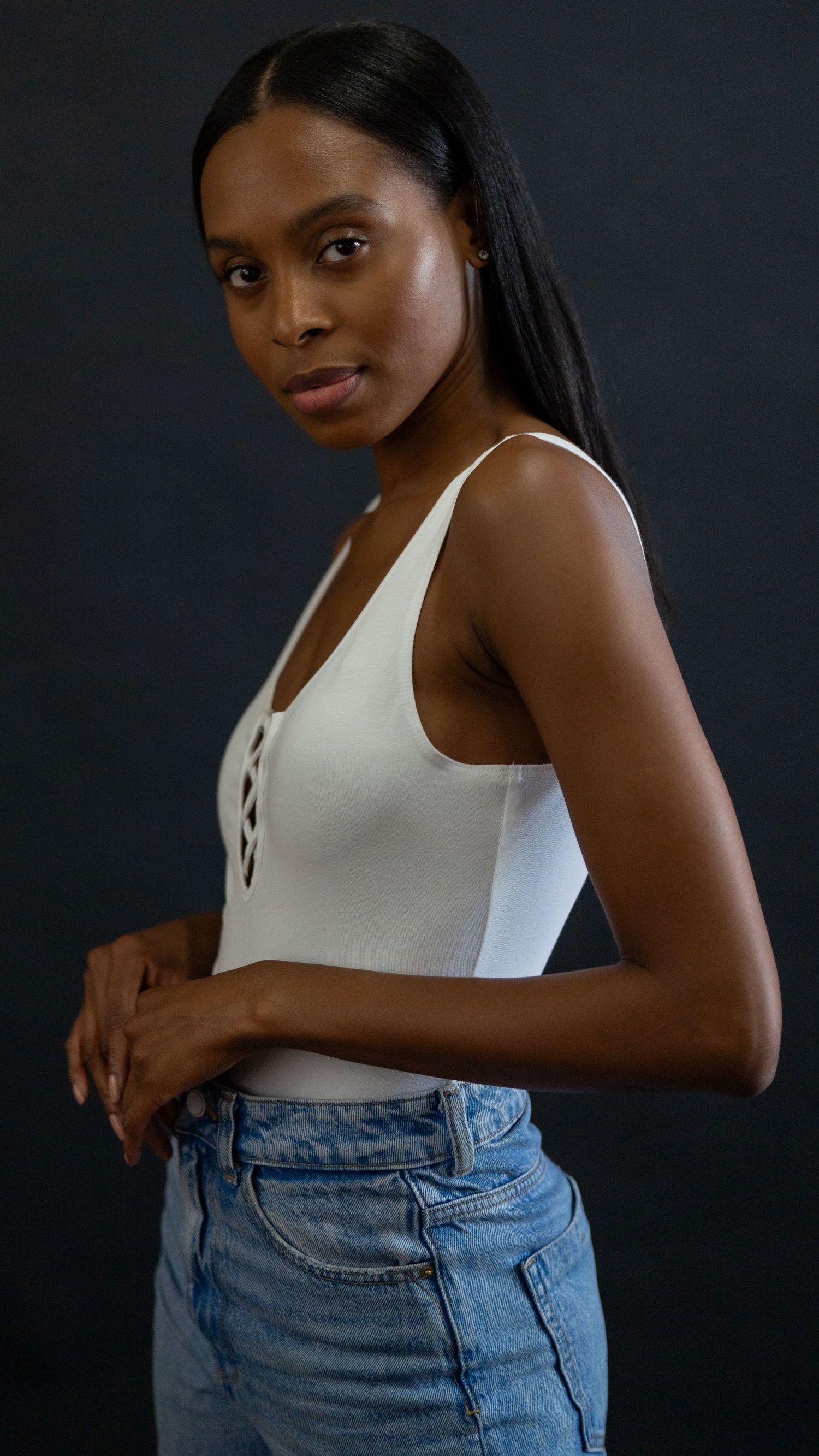 Portrait against dark background wearing white tank top and blue denim jeans in casual pose.