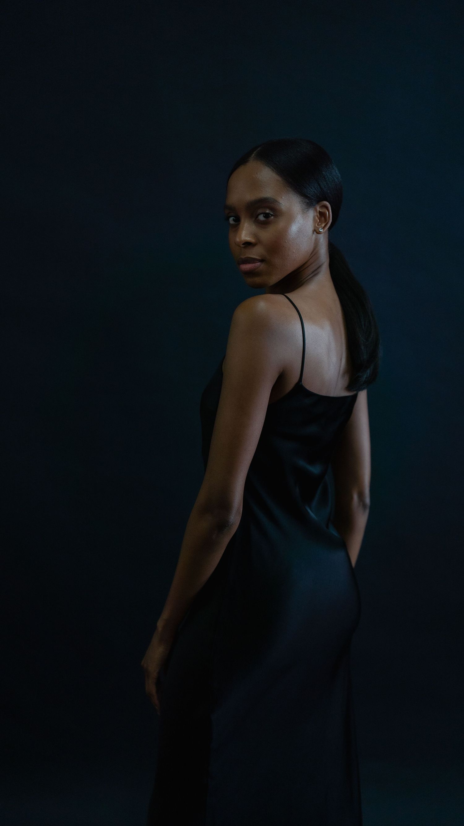 A woman in a black dress poses dramatically against a dark background.