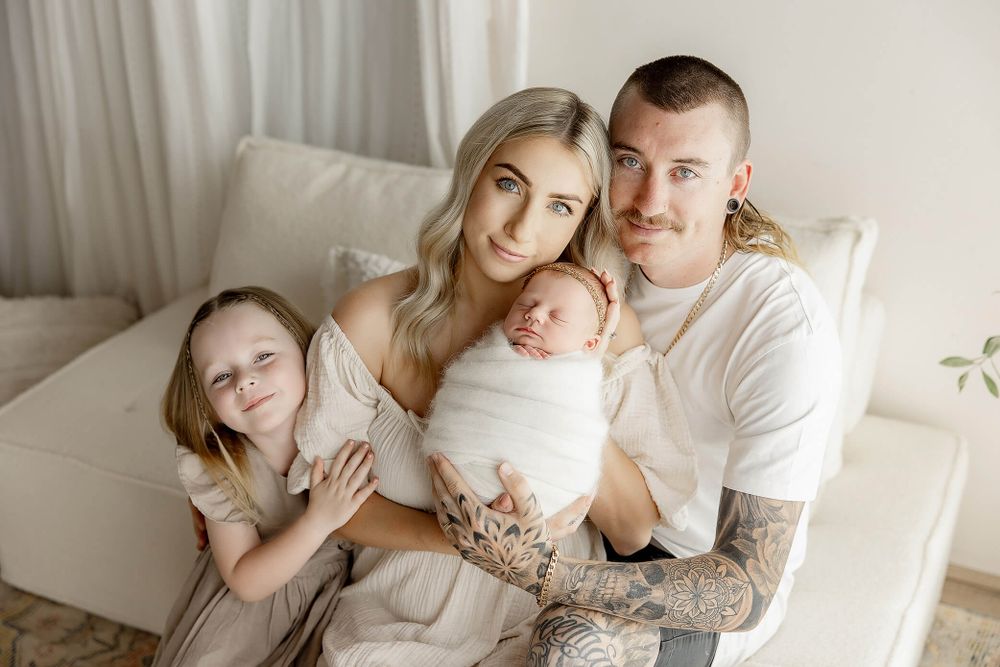 A family sitting together on a white couch in soft natural light for a tender portrait session.