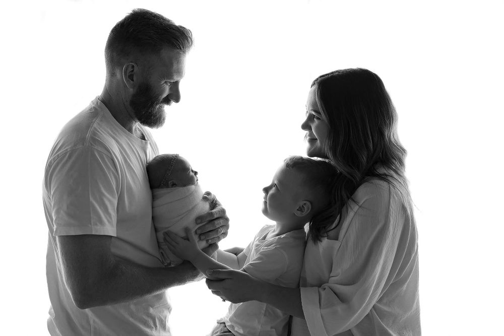 Black and white silhouette of a family bonding together with parents and two small children in tender moment.
