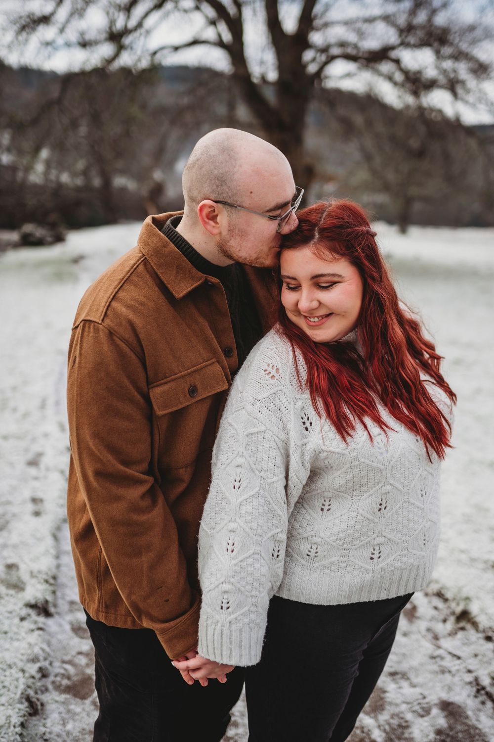 A couple shares tender moments in the snow wearing matching brown and cream colored outfits during a winter photoshoot.