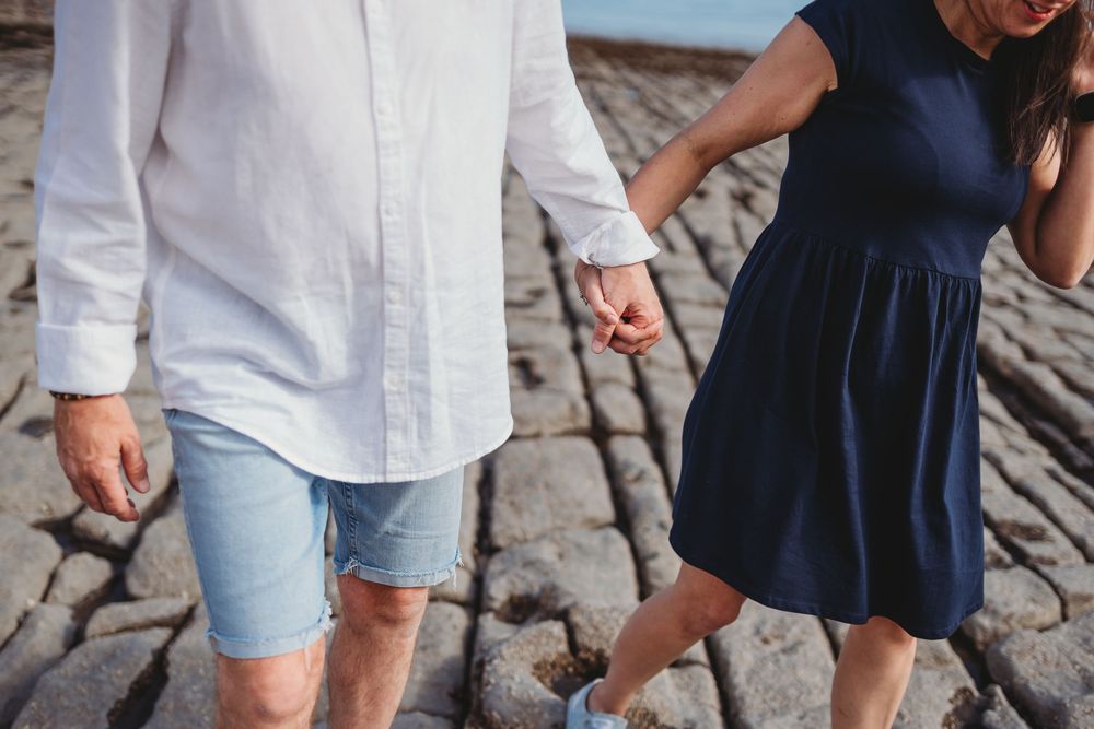 A couple wearing blue and white outfits walks on cobblestone pavement during a sunny day.