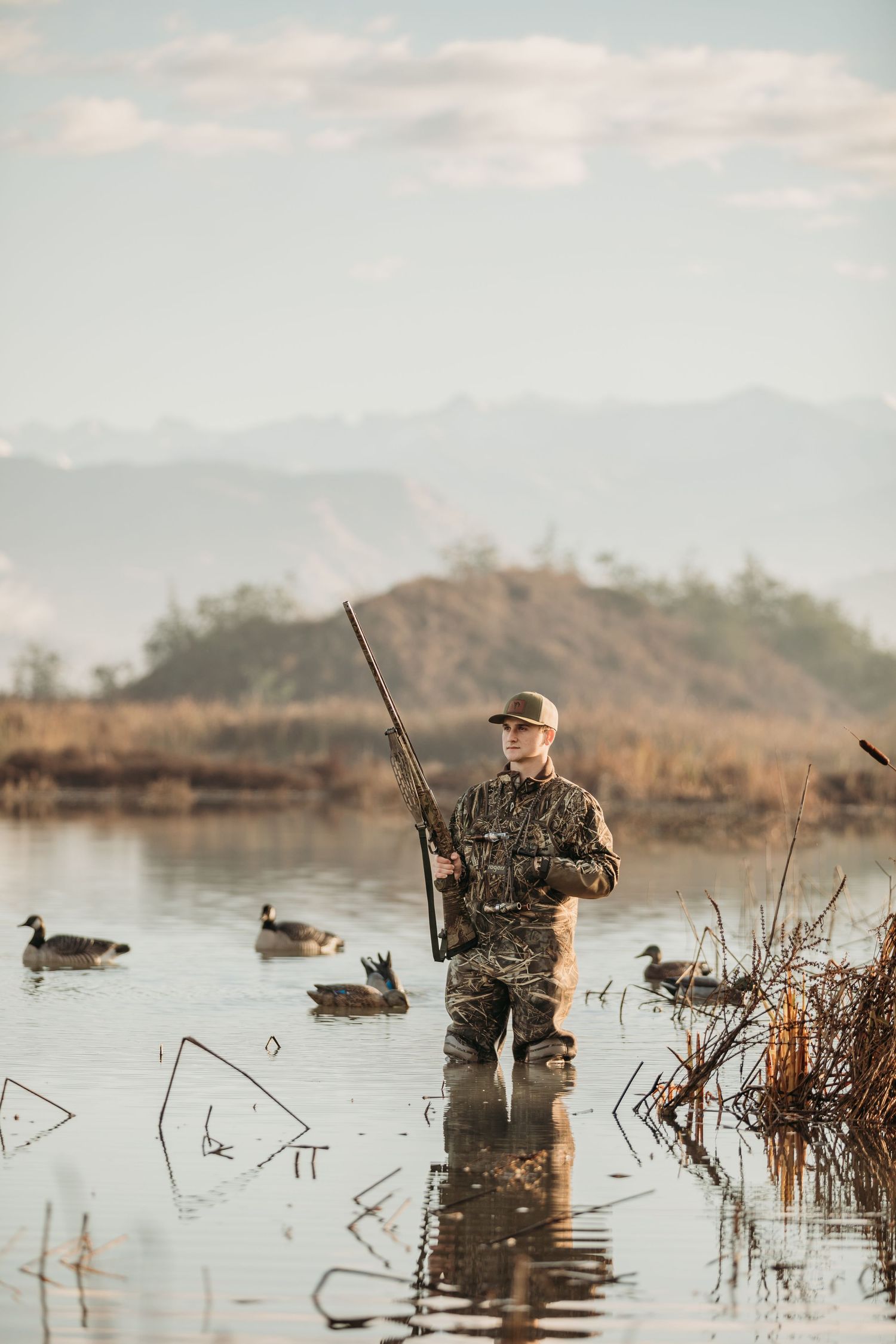 Duck hunter standing in wetland marsh with mountains in background during sunrise.
