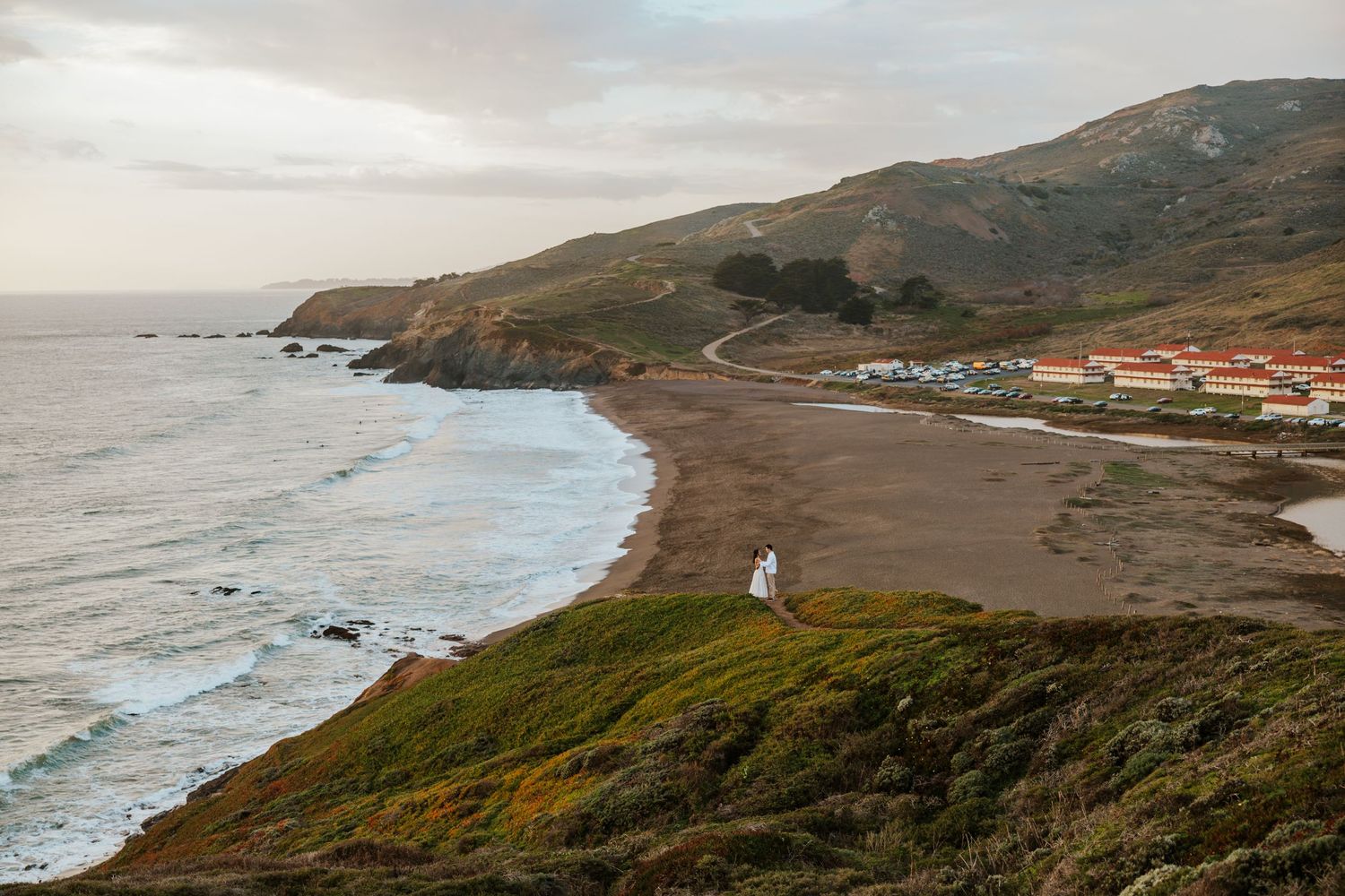 majestic couple standing on cliff in marin headlands with beach, mountains, and cliffs behind them - san francisco engagement photoshoot