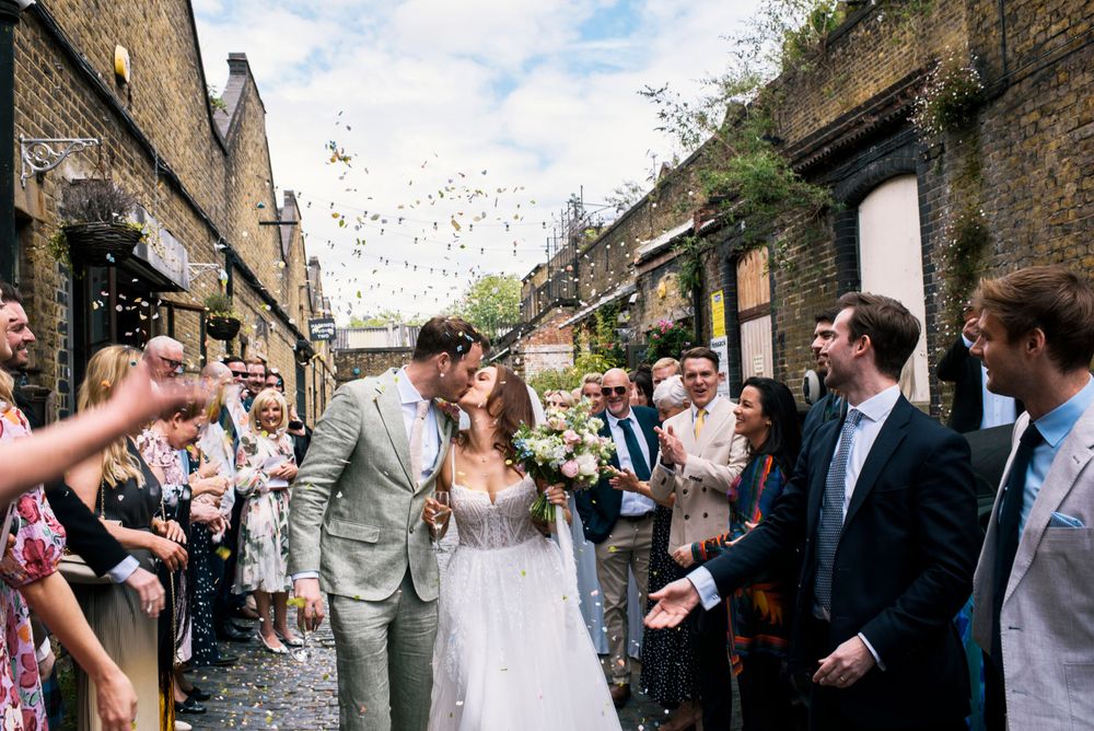 Happy couple exits historic cobblestone venue as guests shower them with confetti on their joyous wedding day.