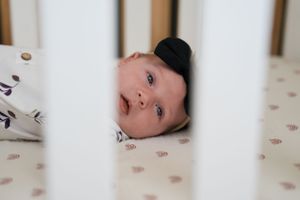 Baby peering through white crib slats in a nursery.