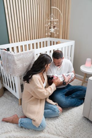 Parents sitting beside white crib while bonding with their newborn.