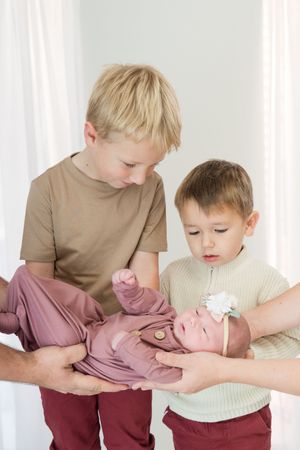 Two siblings in matching brown and burgundy outfits share a tender moment while embracing.