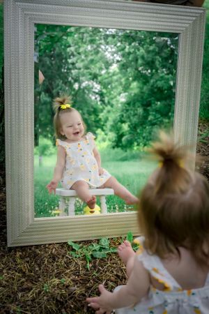 Creative outdoor photo of toddler looking at reflection in ornate white frame.