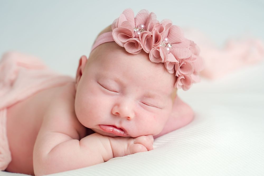 Peaceful sleeping newborn baby wearing pink floral headband resting on soft white blanket.