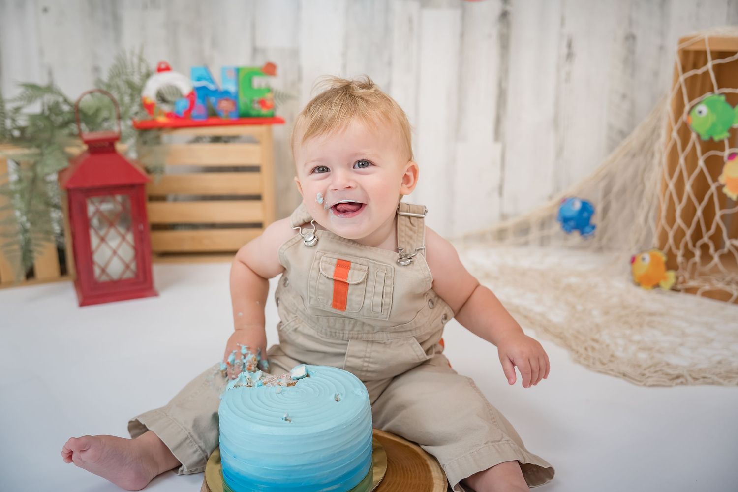 A first birthday party celebration with a blue and white cake, decorative lanterns, and rustic wooden accents.